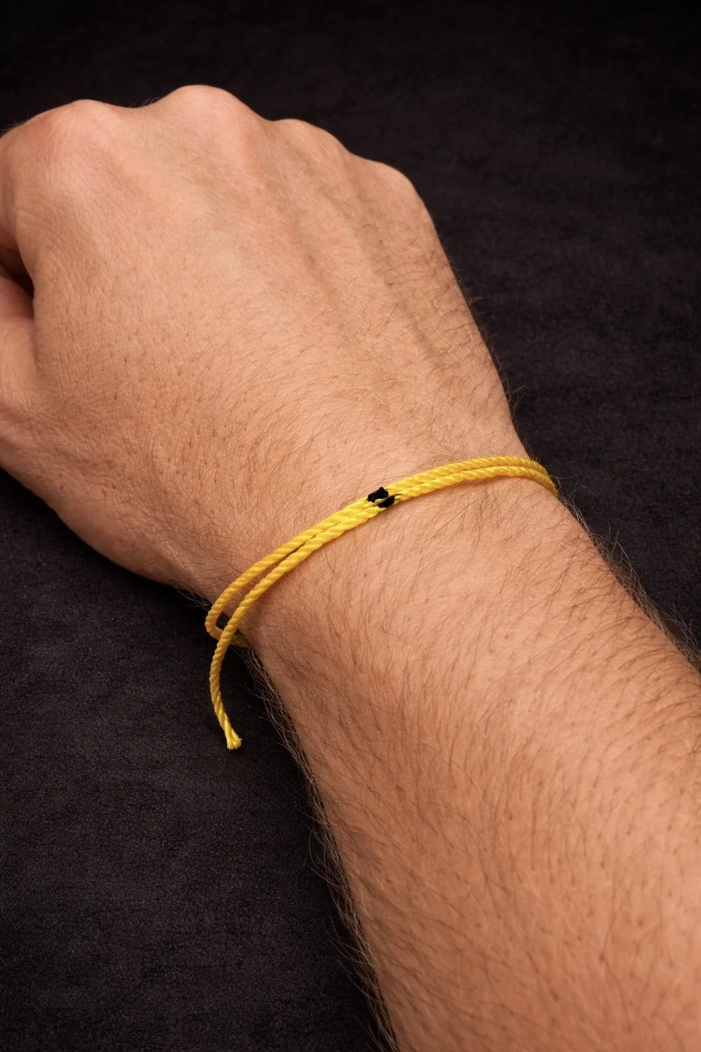 A person's wrist and hand with a yellow string featuring black marker marakings, resting on a black surface.