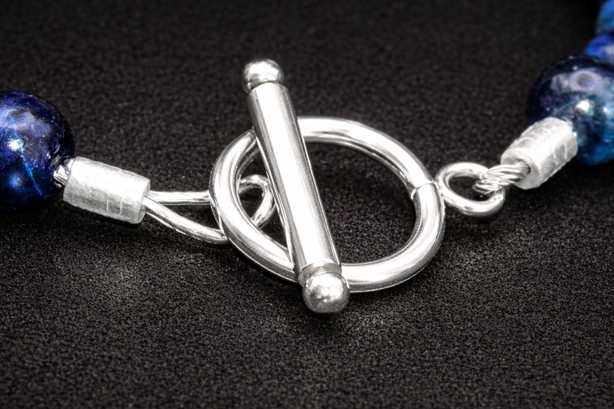 A close-up of a silver toggle clasp on a necklace with blue beads.