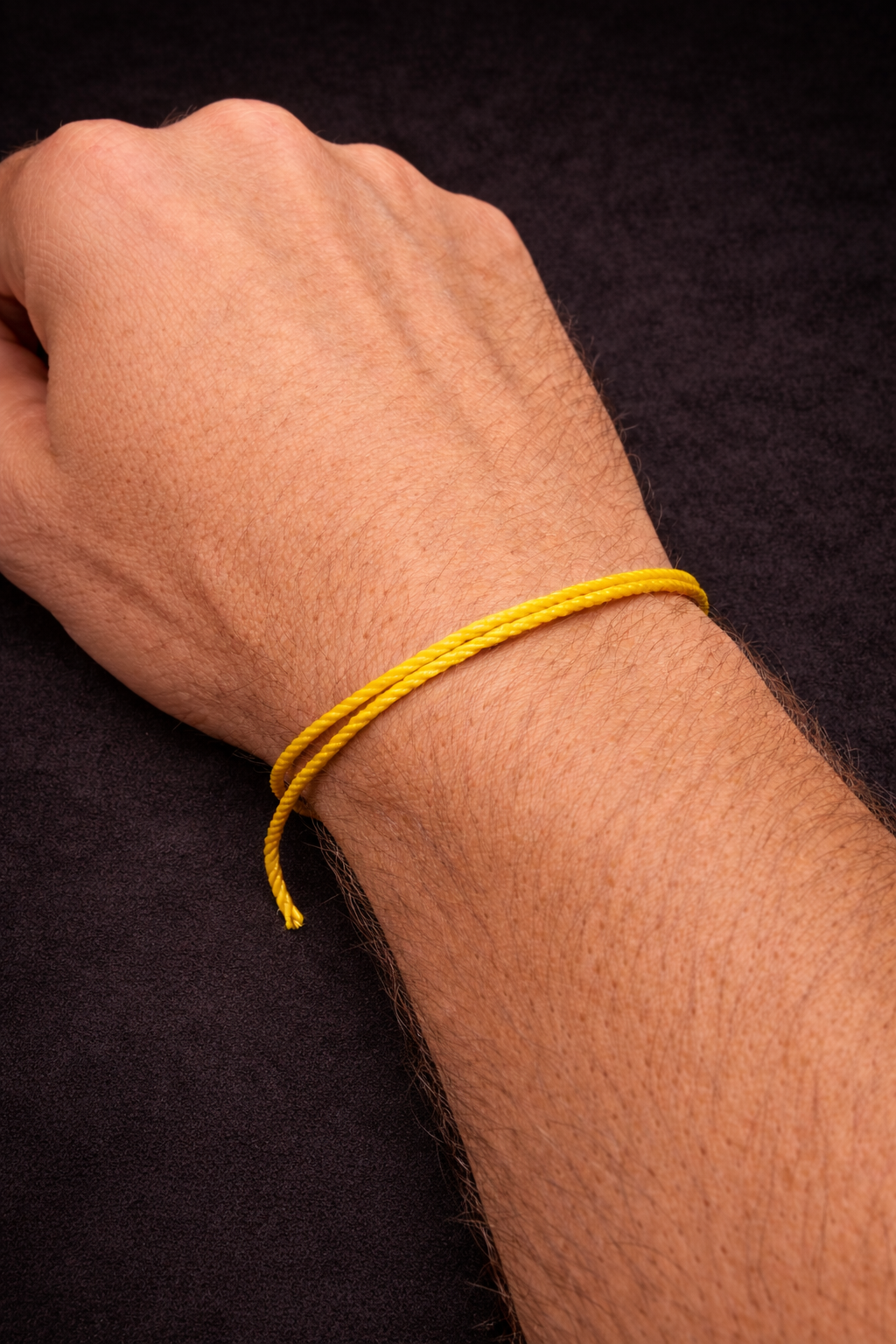 A close-up of a person's clenched fist wearing a yellow string to be used as a tool to measure and mark, resting on a black surface.