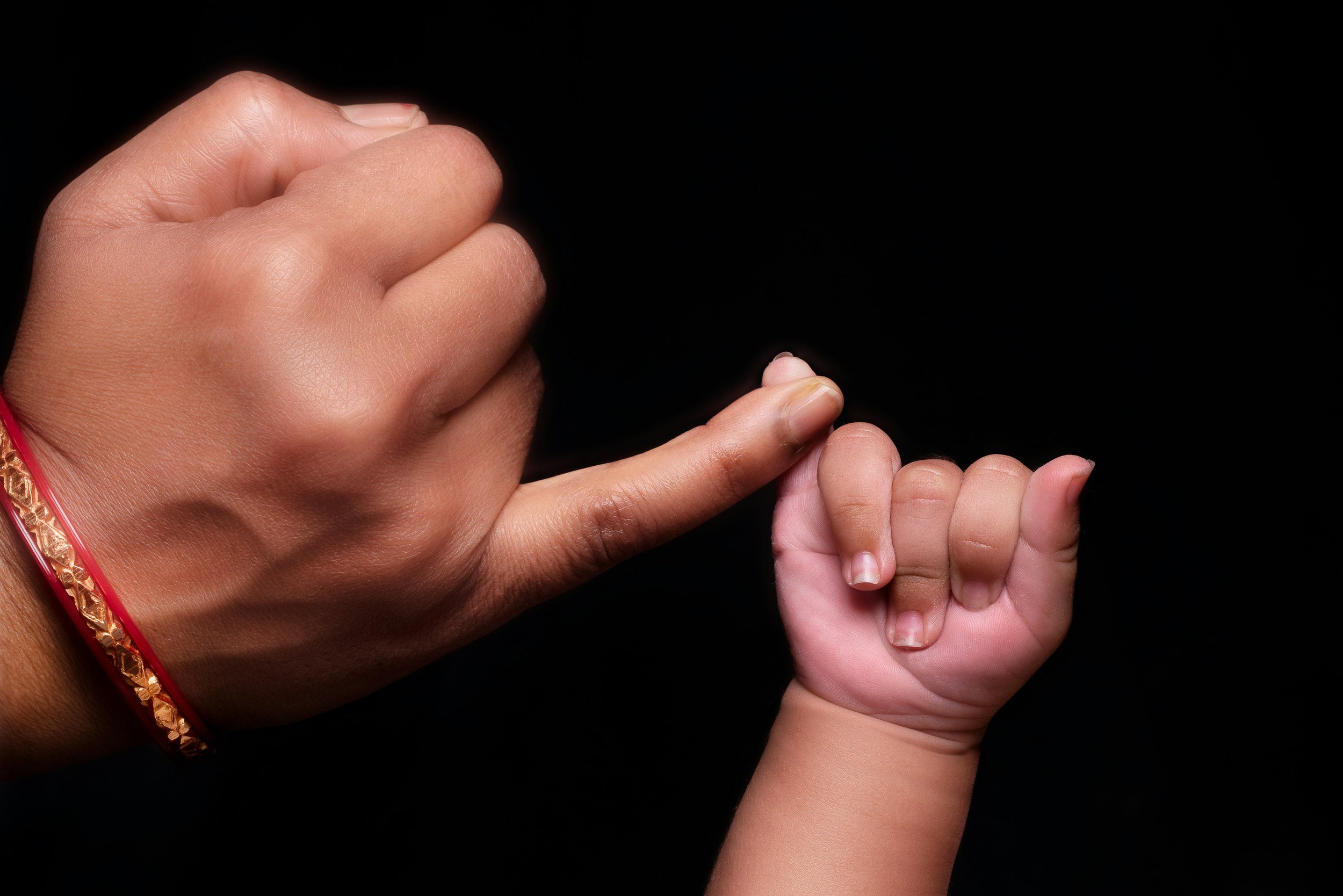 Newborn baby’s pinky finger gently touching a parent’s finger, symbolizing love and family connection.