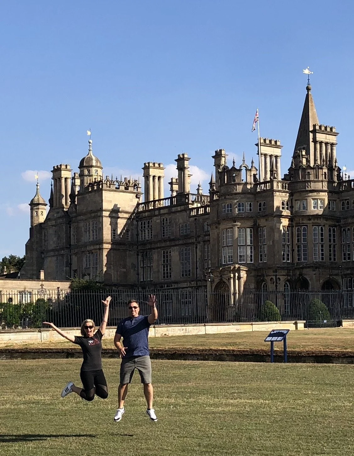Two people jumping in front of a historic castle with a clear blue sky in the background.