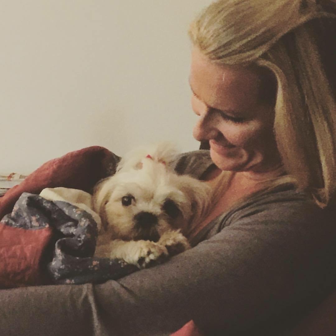 A woman is cuddling a small, light-colored puppy in her arms, both appearing content and affectionate.