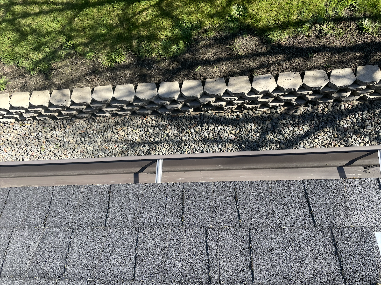 Roof shingles, metal railing, gravel, rocks, grass, and soil in a landscaped area.
