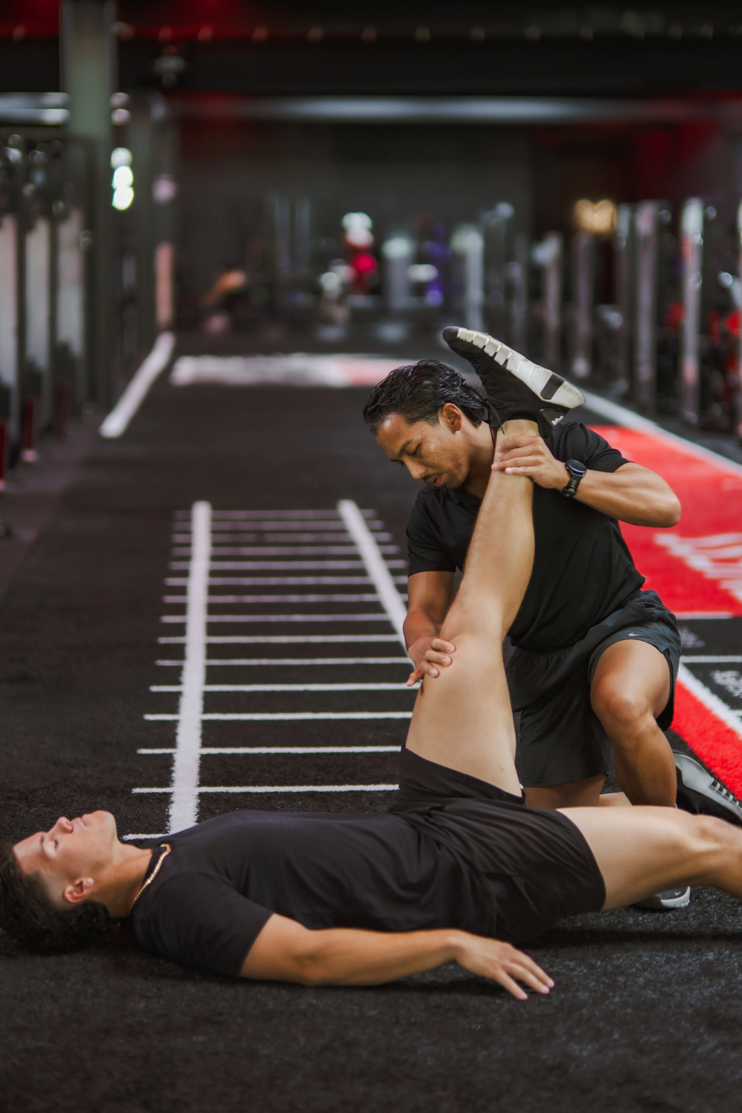 Trainer assisting a person in stretching exercises in a gym.