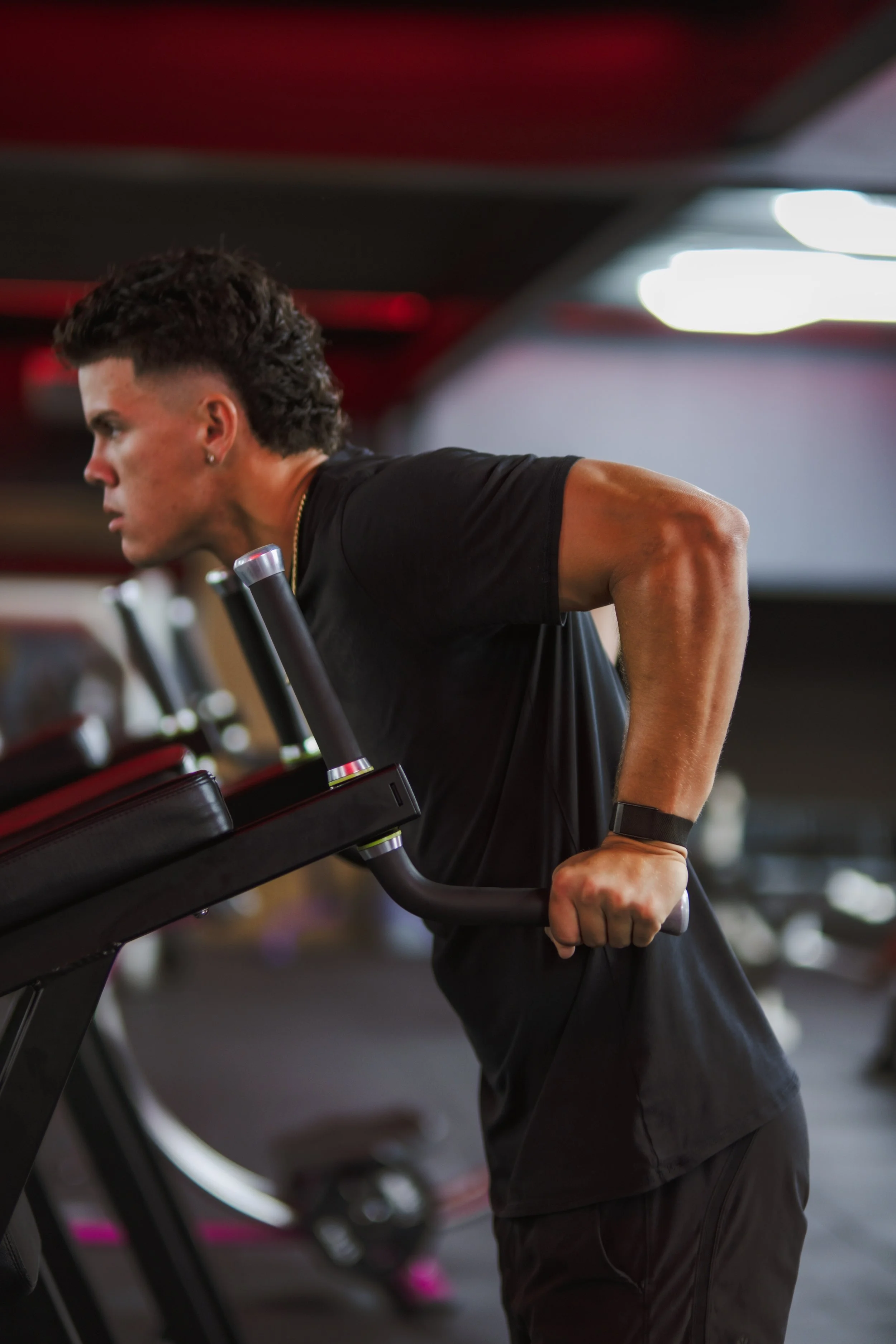 A man in black workout clothes is doing a dip exercise on parallel bars in a gym, with a focused expression on his face.