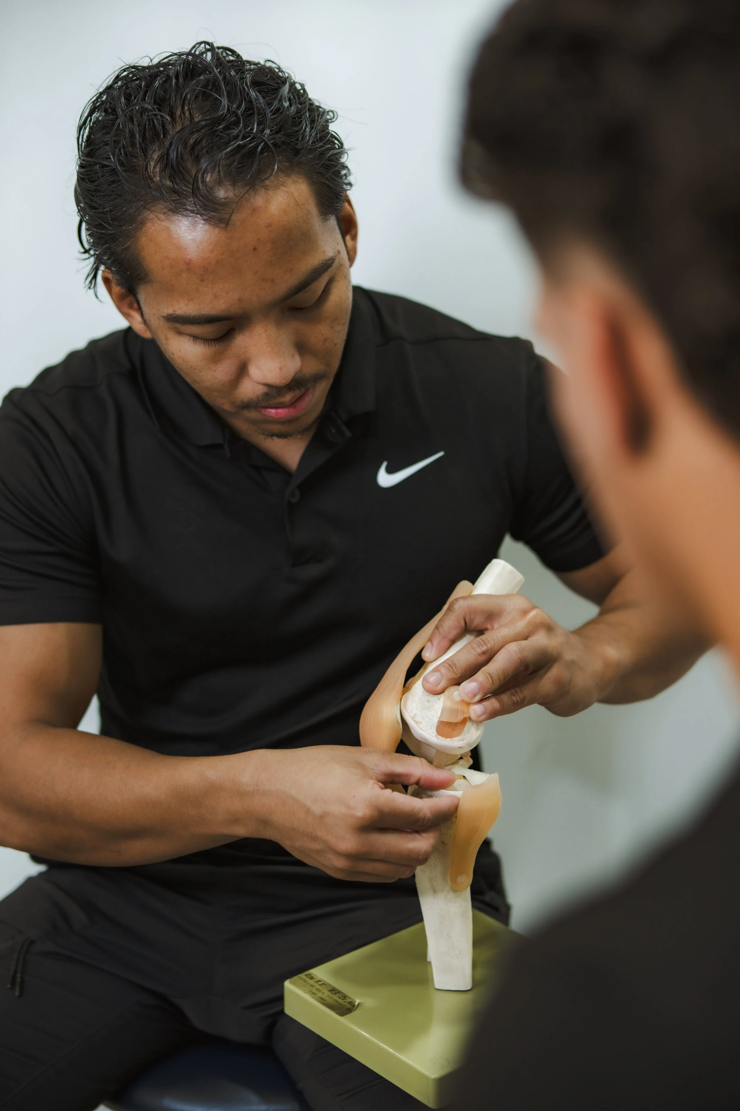 A young man in a black Nike shirt using anatomical models of a human leg and pelvis for educational purposes in a classroom or medical training setting.