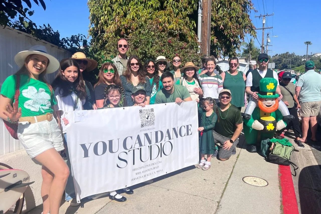 YCD Studio team posing with the studio banner at the 2026 St. Patrick’s Day Parade in Hermosa Beach