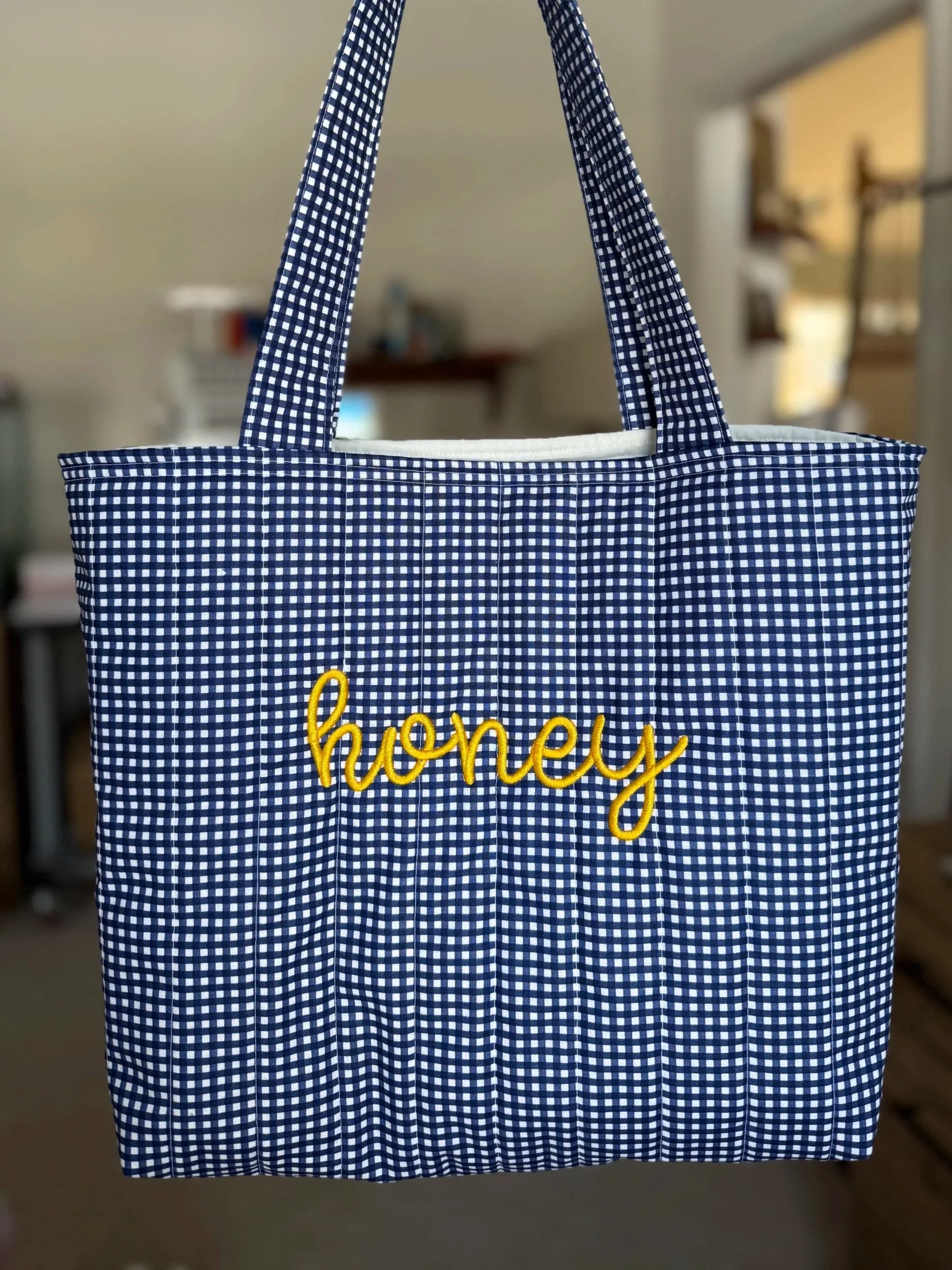 A blue and white checkered tote bag with the word 'honey' embroidered in yellow on the front.