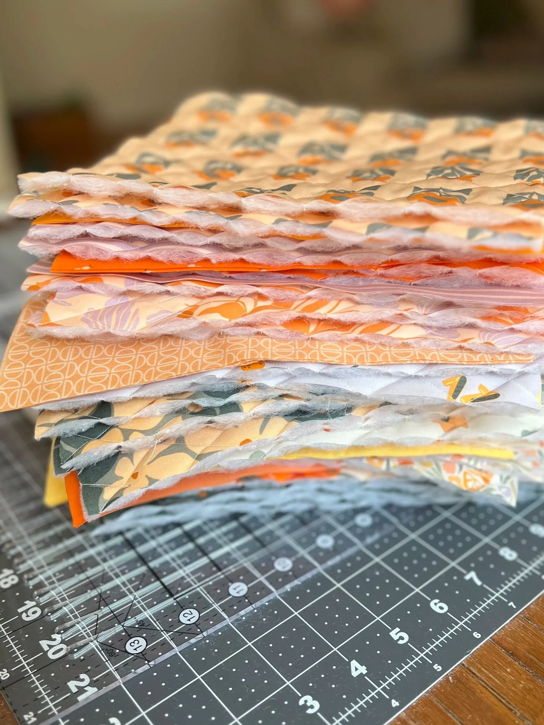 Stacked fabric pieces with various patterns and textures on a cutting mat.