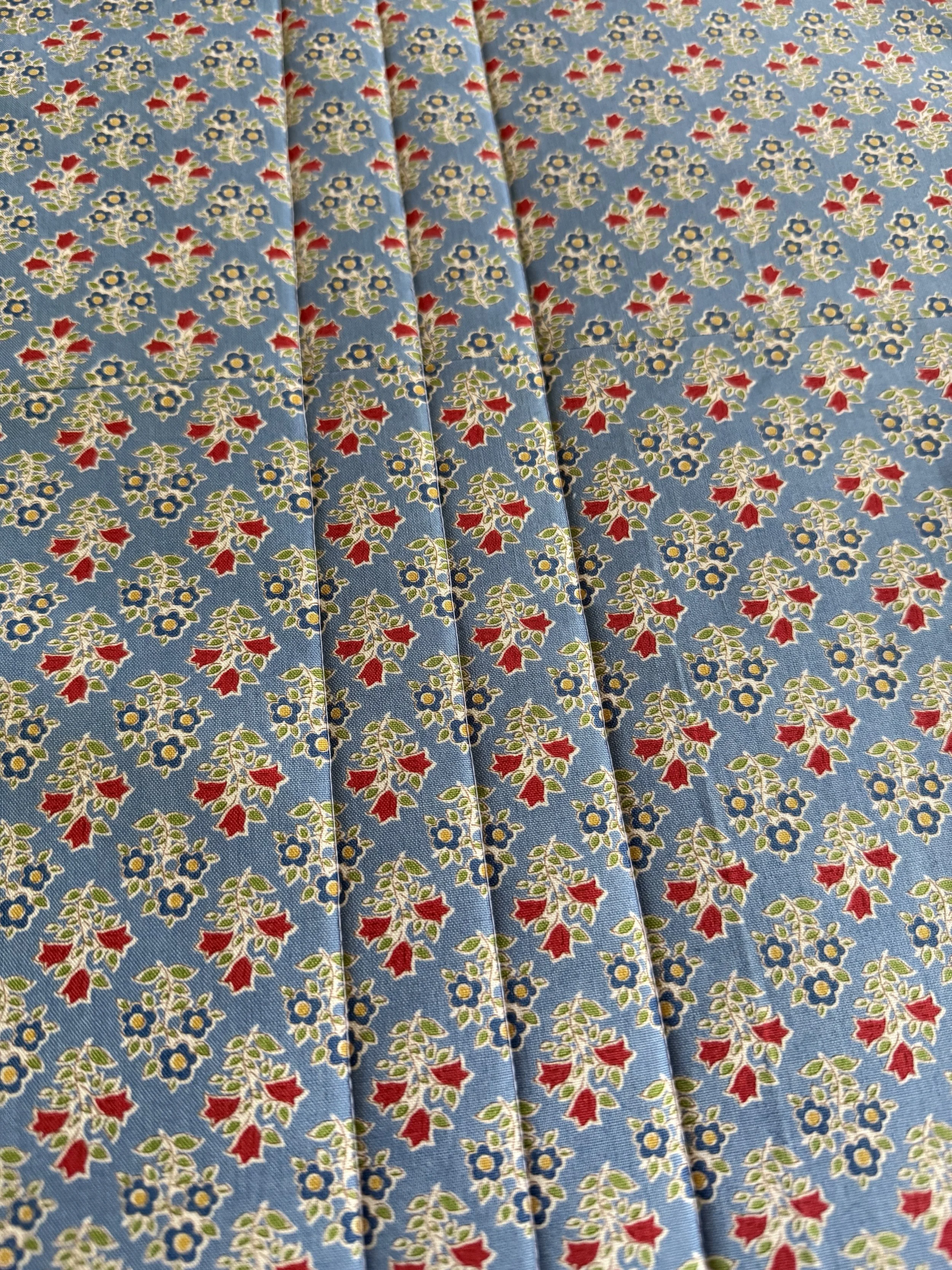 Close-up of blue fabric with small floral pattern featuring red, yellow, and white flowers.
