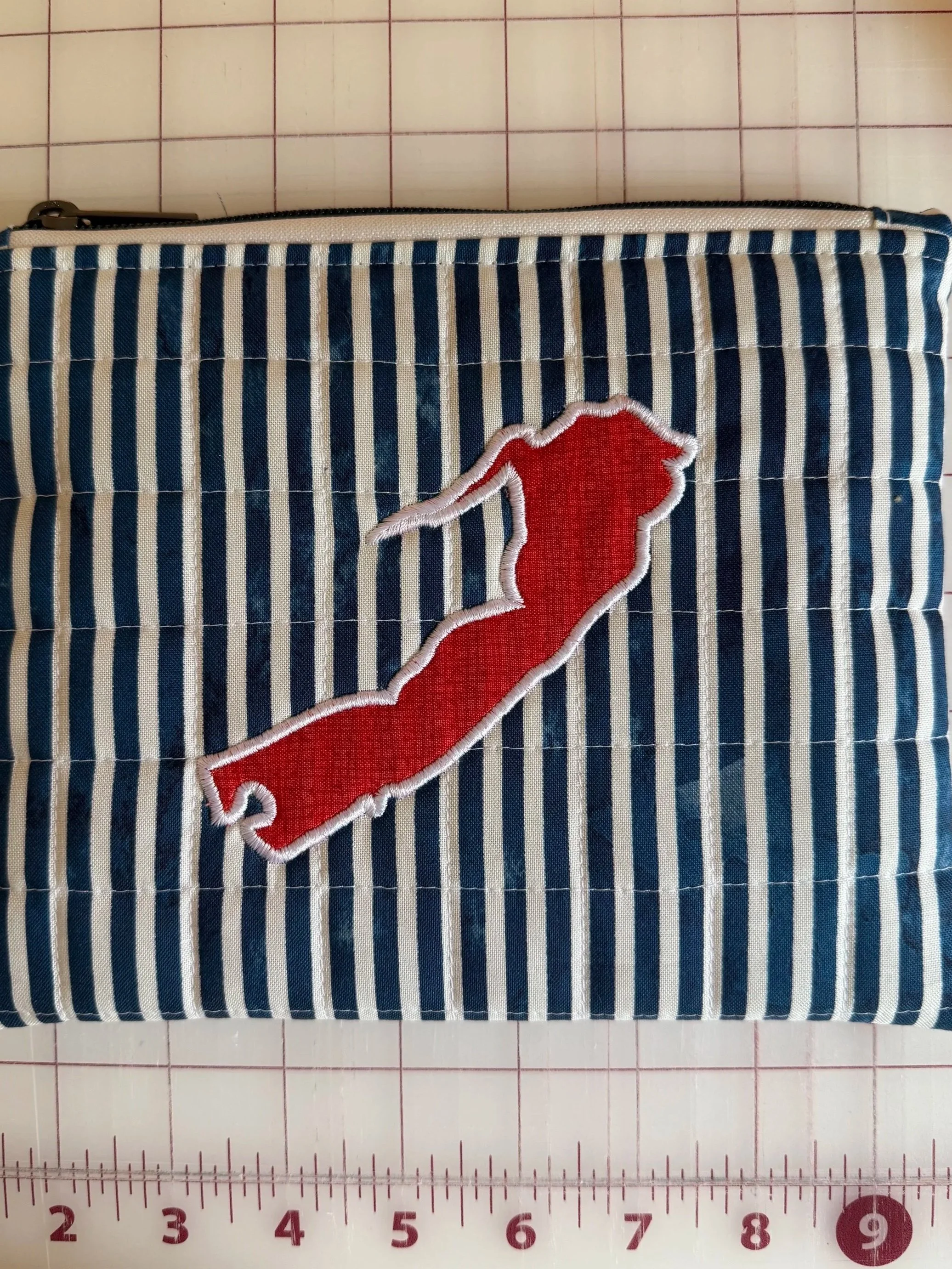 A striped fabric pouch with an embroidered red chili pepper patch on the front.