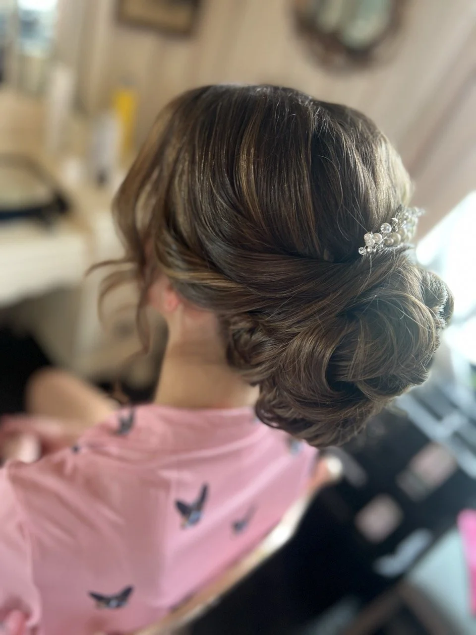 Back view of a woman with styled brown hair adorned with a pearl and crystal hair accessory in an indoor room.