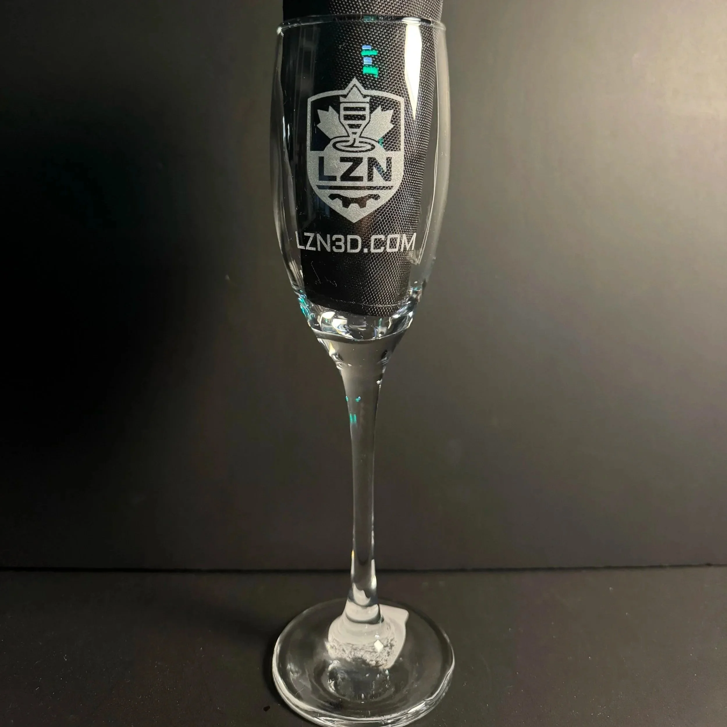 Une flute en verre avec une gravure blanche portant le logo de LZN comportant une feuille d'érable avec l'inscription LZN et le site web LZN3D.COM.