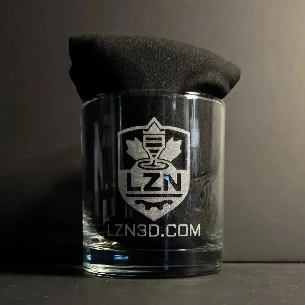Un verre à whisky avec le logo LZN gravé dessus, posé sur une surface noire.
