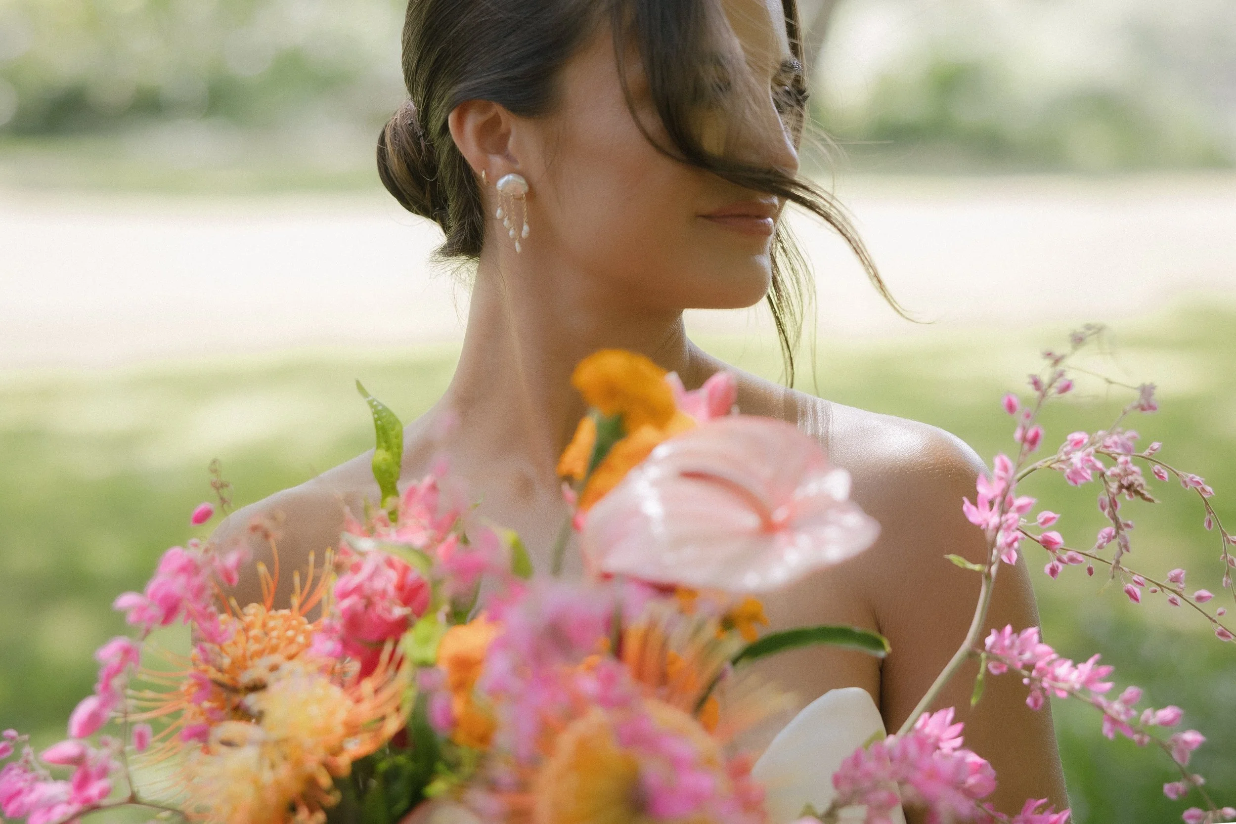 Bride holding colorful bouquet in Oahu, Hawaii, natural light bridal portrait highlighting pearl earrings and bespoke bridal details.