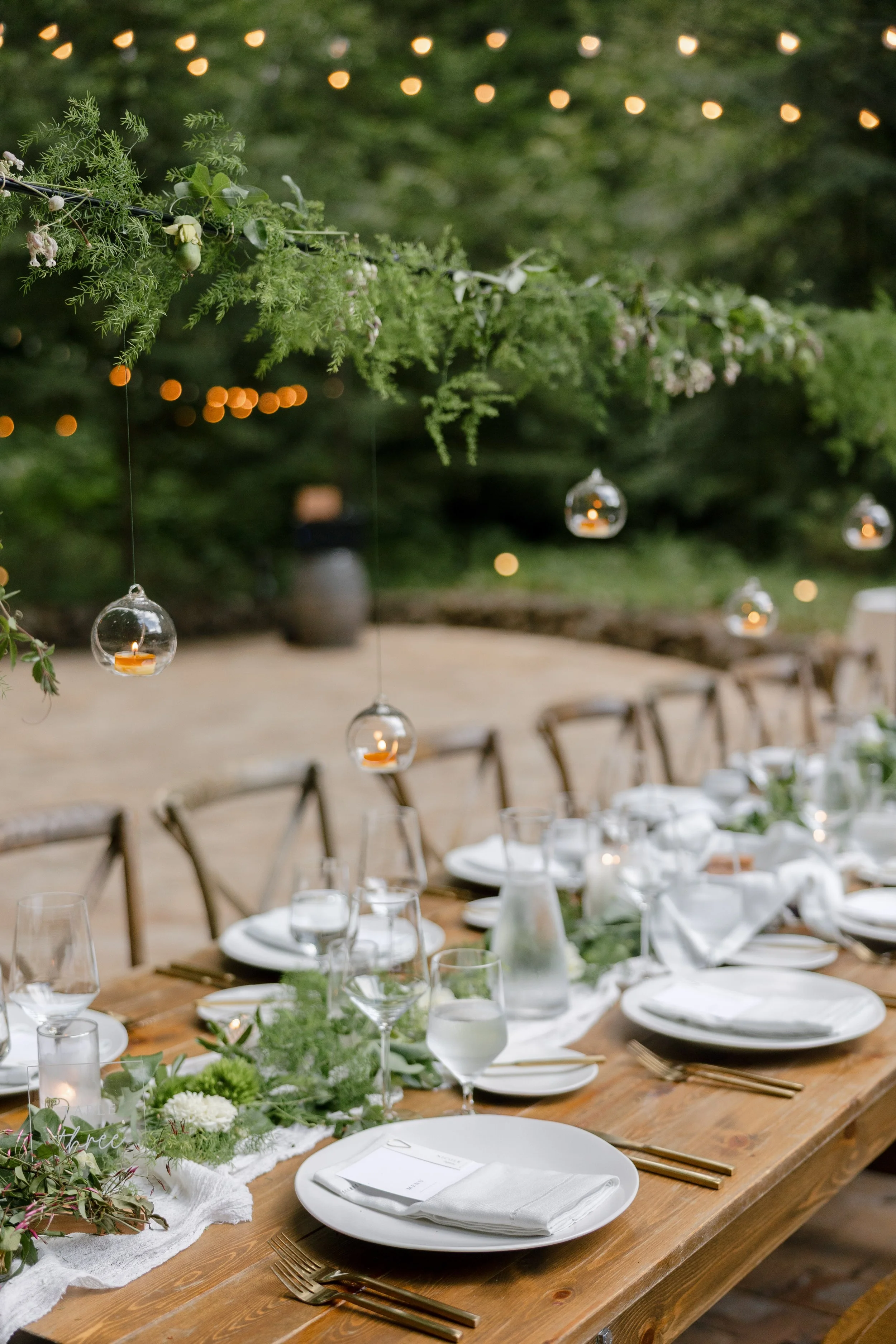Luxury wedding tablescape with hanging glass candle installations and greenery, unique reception table design inspiration.