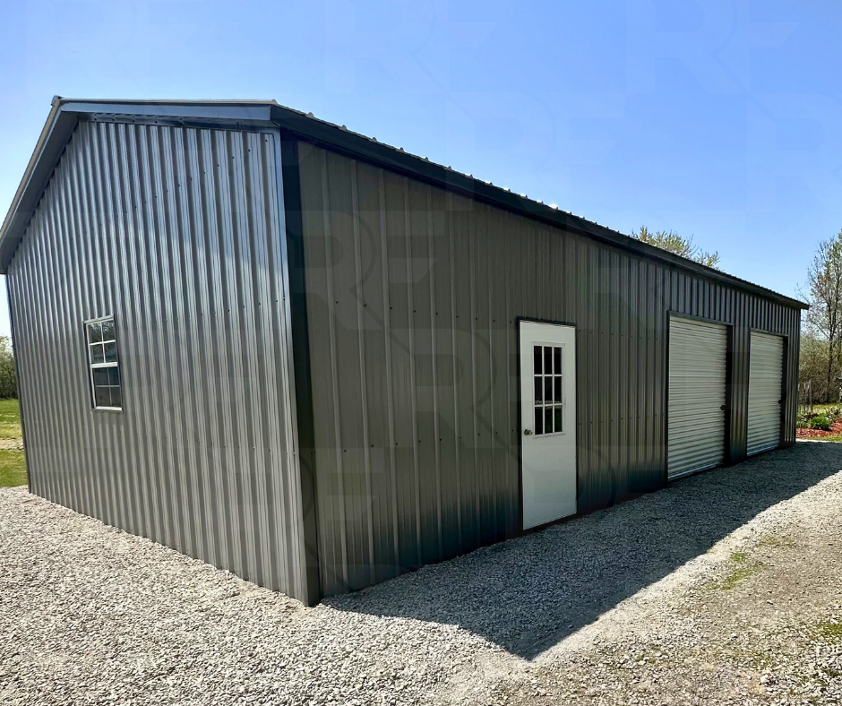 A 24x40 2 bay large metal storage building with a grey exterior, one side door with a window and two roll-up garage doors, situated on a gravel lot with a grassy background.