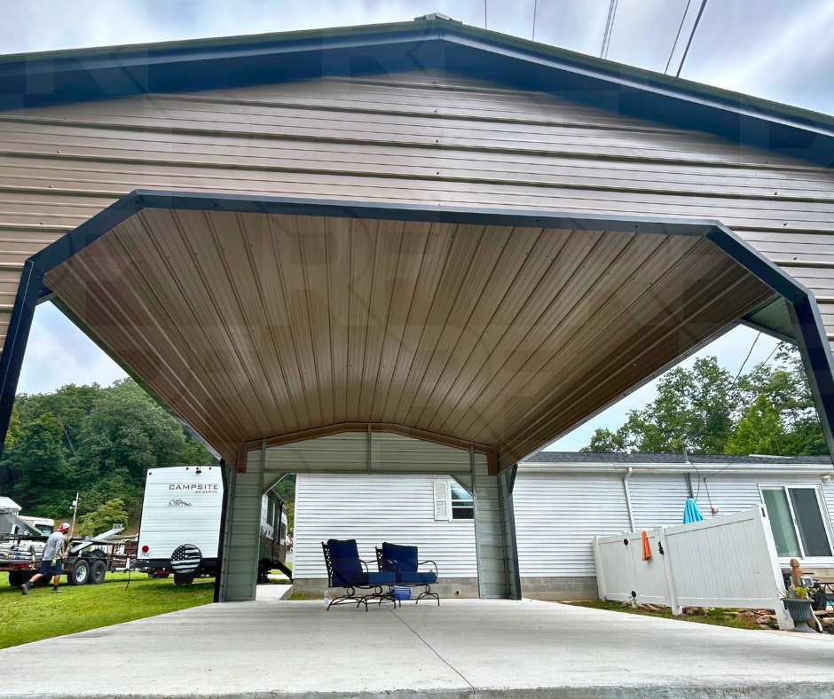 View of a covered carport with two chairs underneath, attached to a white house with a trailer and a person in the background.
