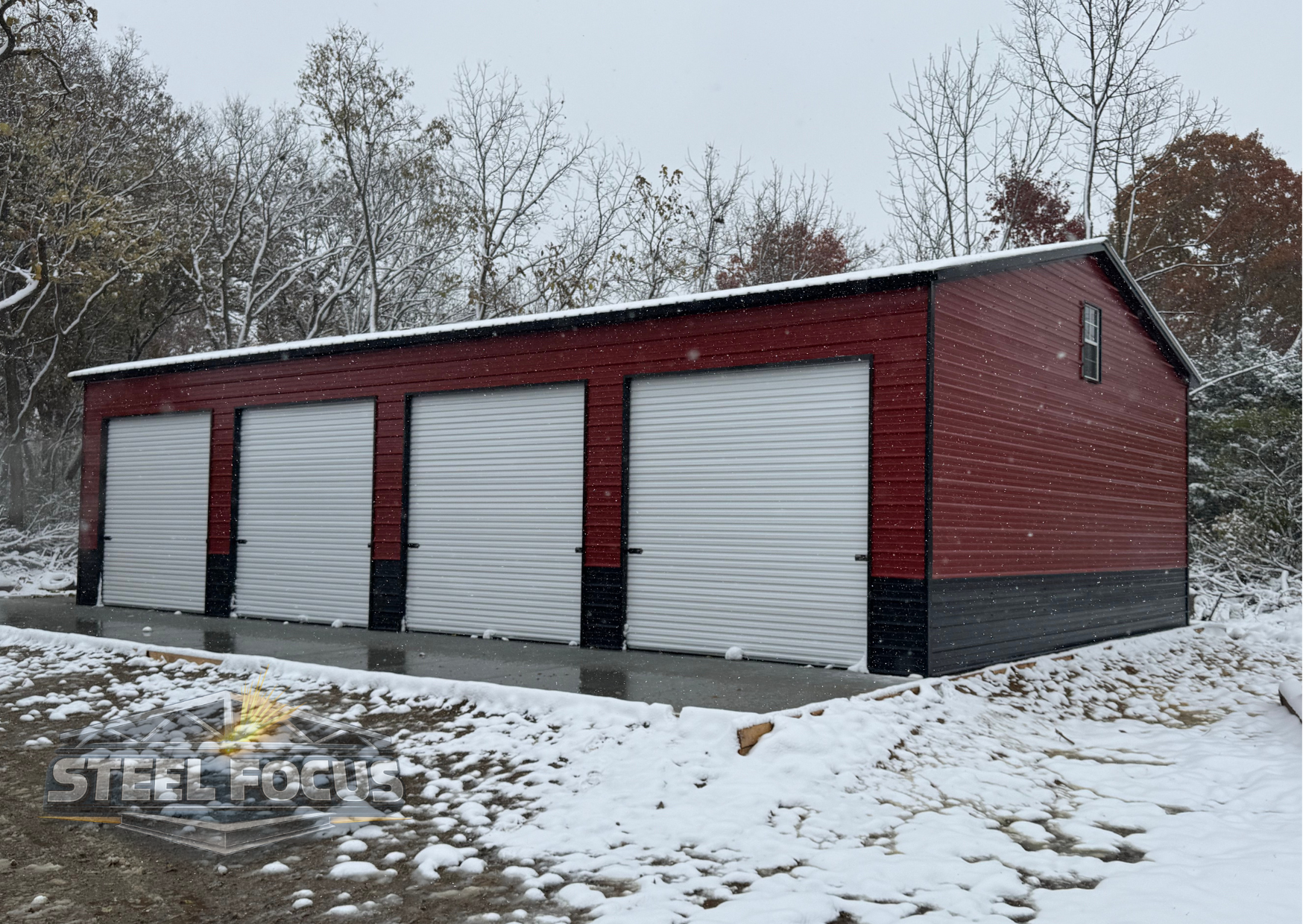 A red storage building with four white roll-up garage doors and black trim, situated outdoors on a partly snow-covered ground with snow falling, trees in the background, and a small window on the upper right side.