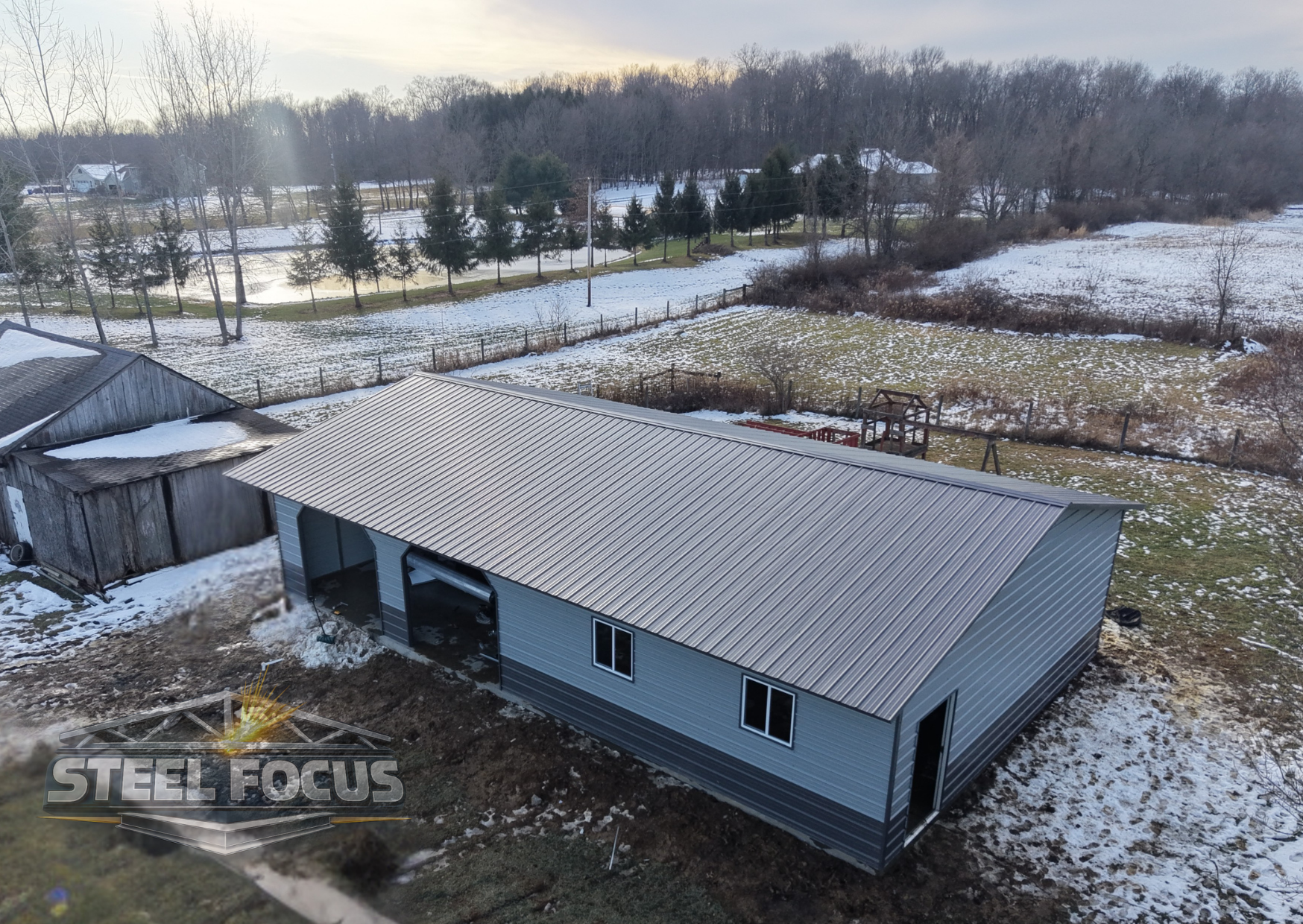 A new metal building with a curved roof in a backyard with snow on the ground and some trees in the background.