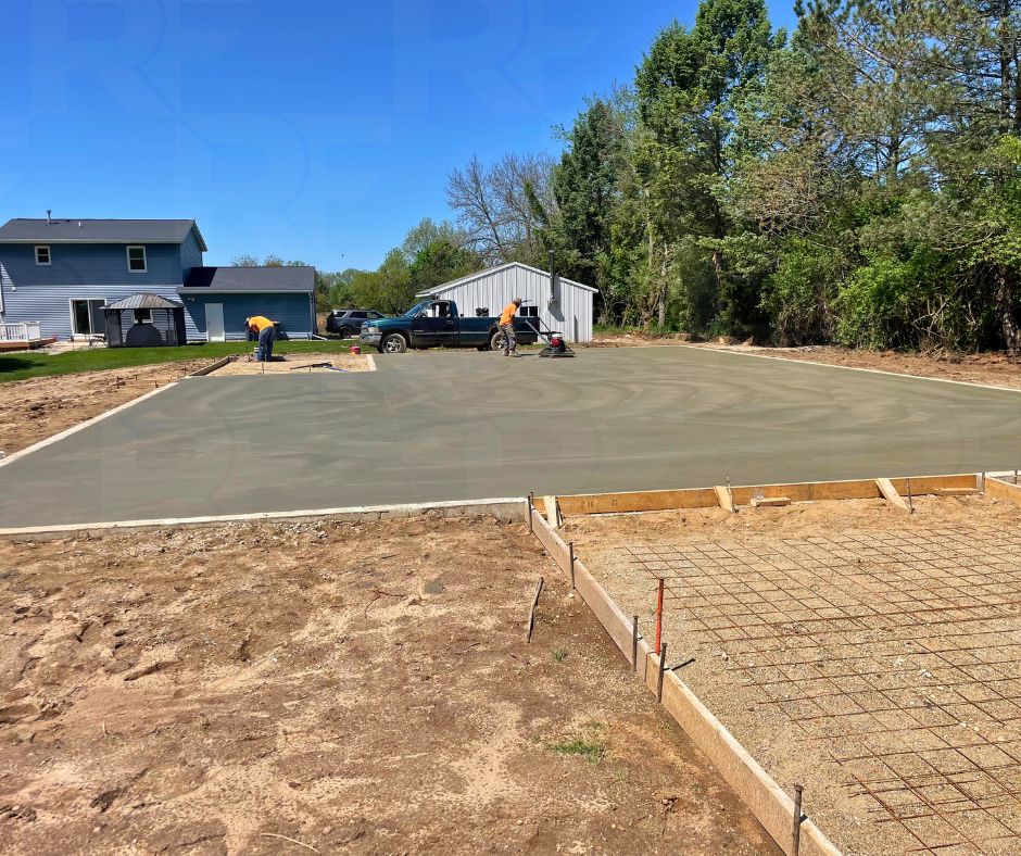 Workers leveling fresh concrete pour for a driveway with surrounding wooden framing on a residential property.