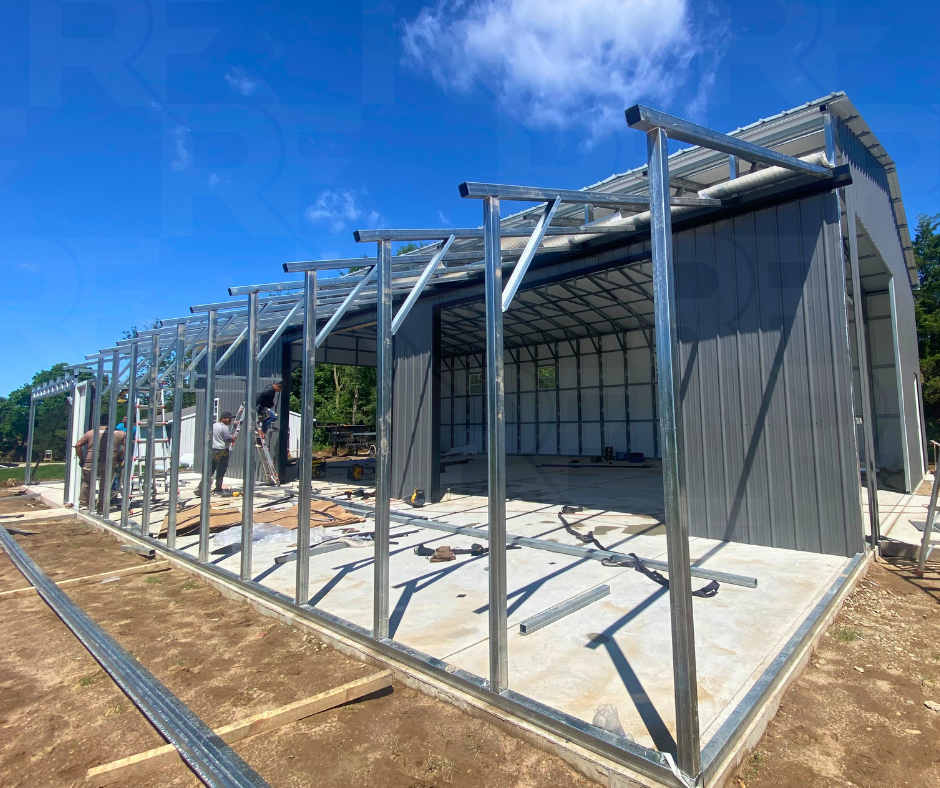 Construction of a metal building with workers assembling the frame under a bright blue sky.