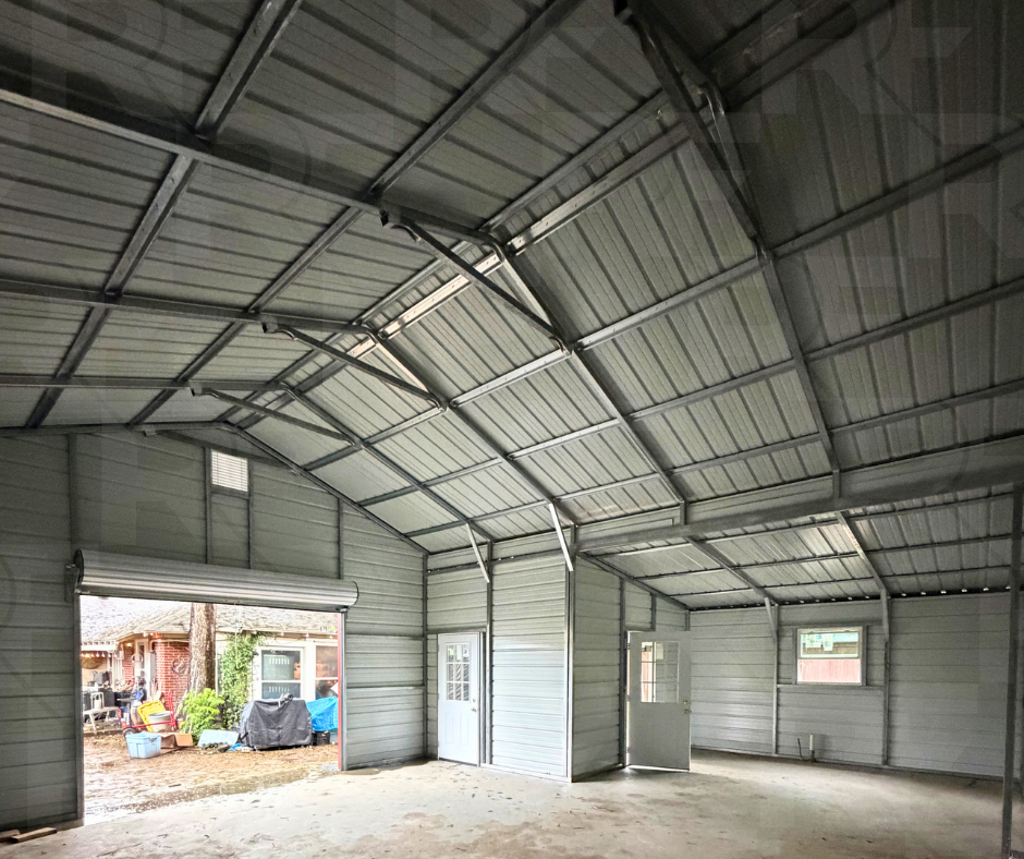 Empty metal garage or shed interior with a partially open large garage door showing outdoor yard with tools, containers, and a covered barbecue grill.