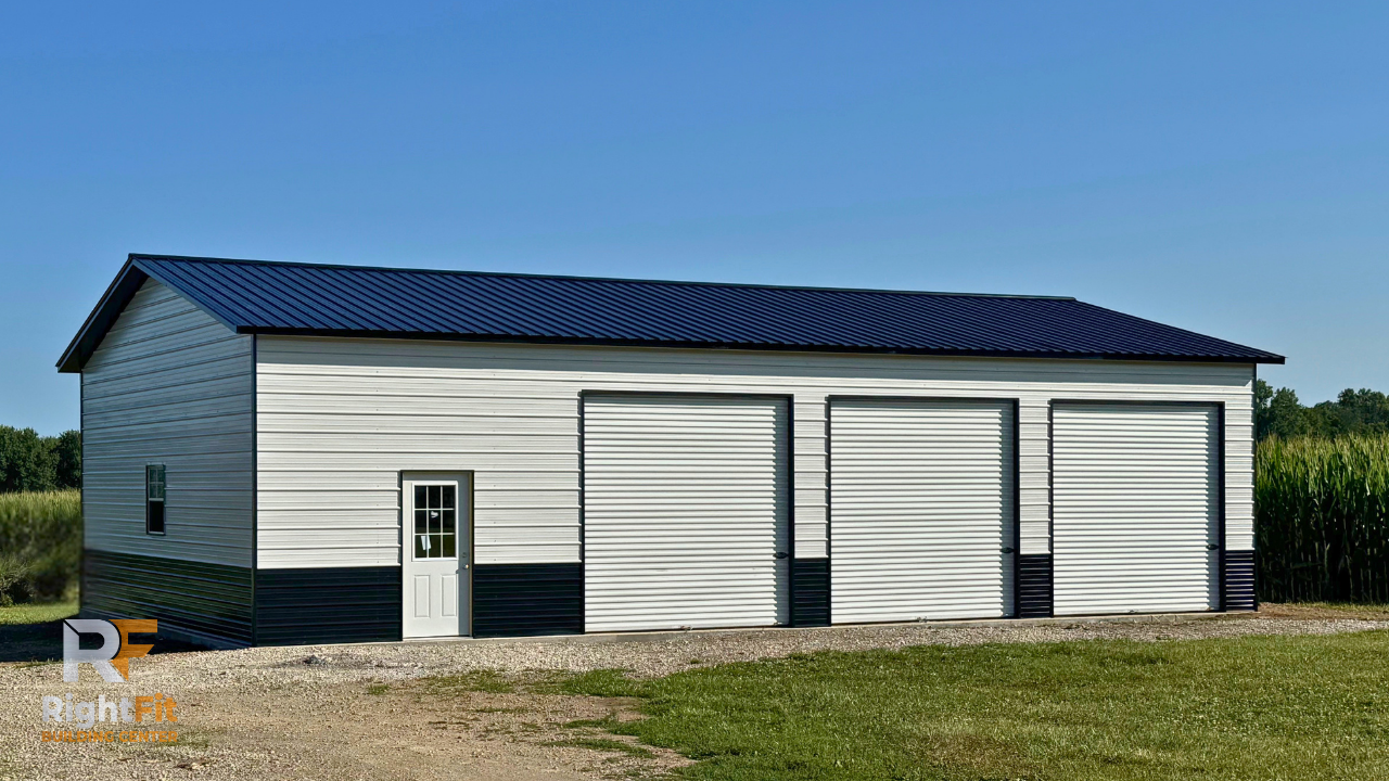A white and black metal storage building with three garage doors, a small door with a window, and a blue metal roof, located in a rural area.