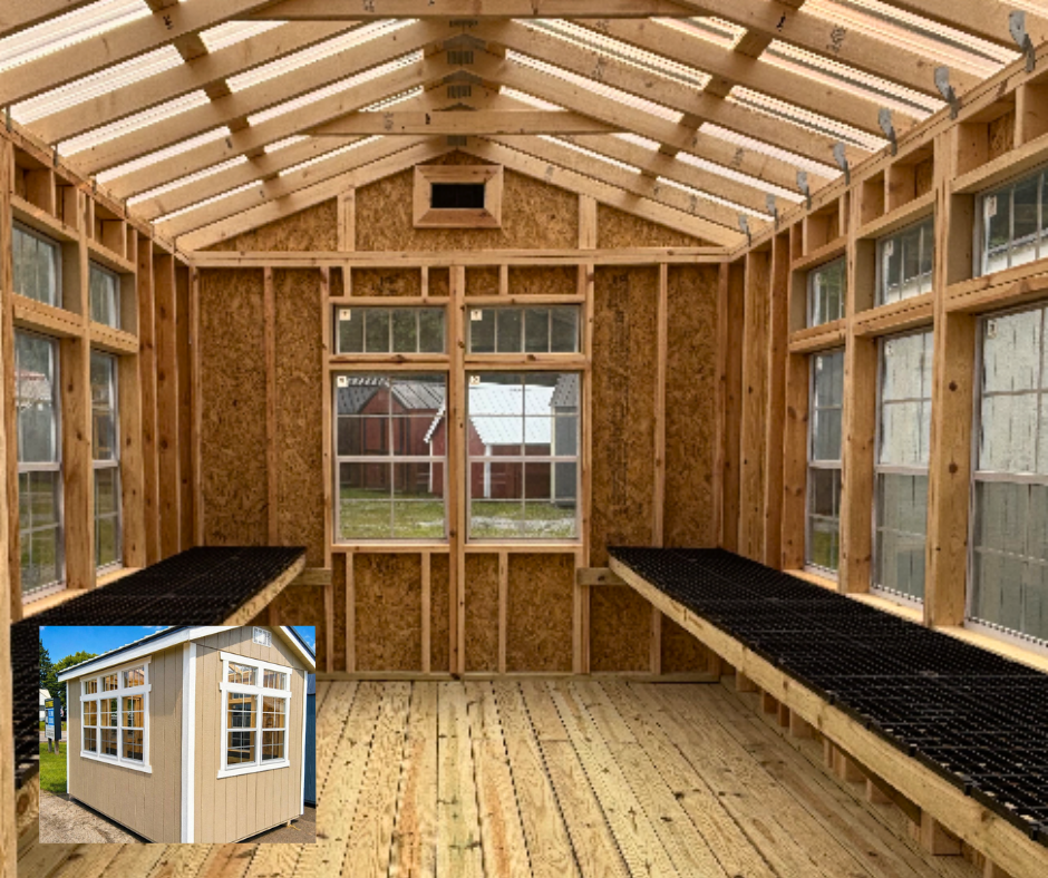 Interior of a small wooden greenhouse under construction with uncovered rafters, walls framed with plywood, and two black bench-like structures along the sides. A small inset image shows the finished exterior of the greenhouse with a beige siding, white trim, and multiple windows.