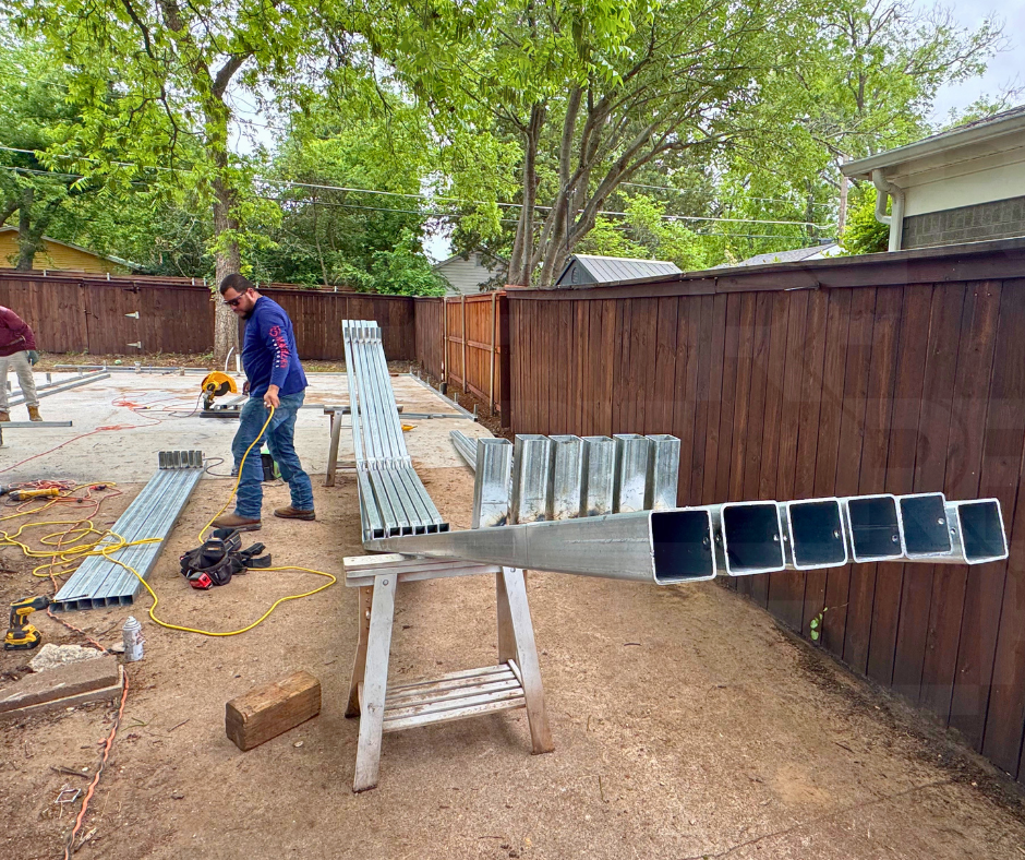 Workers building a metal structure in a backyard with trees and a wooden fence.