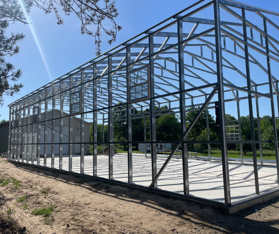Steel frame structure of a building under construction with clear blue sky and trees in the background.