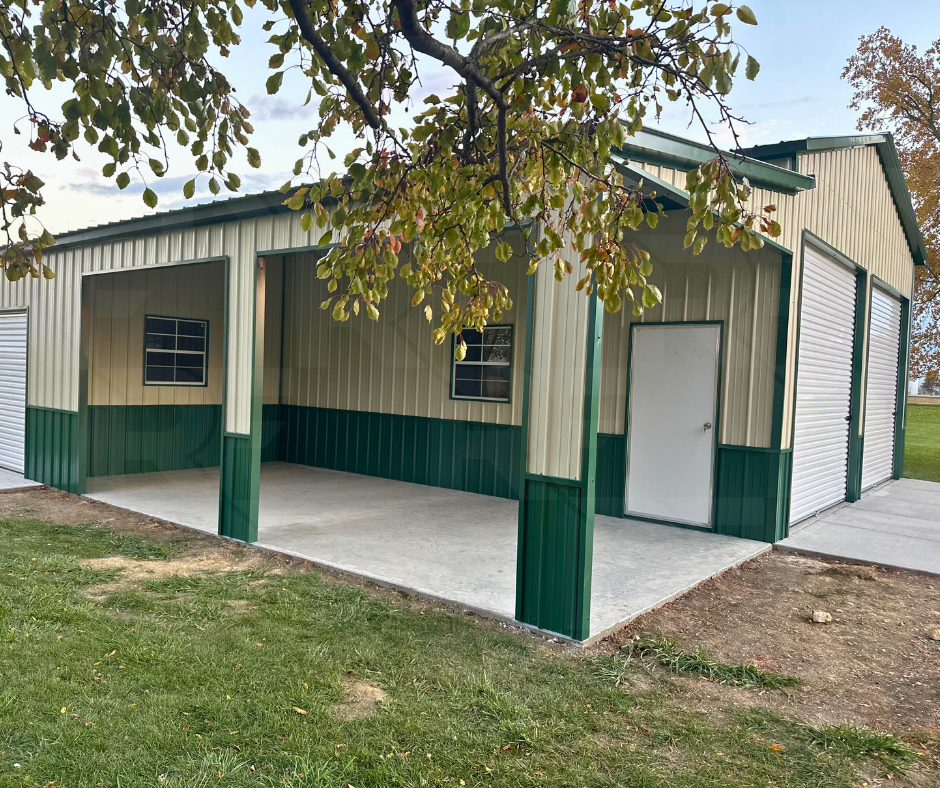 A metal storage building with a partially open garage door, a closed door, and two windows, situated on a concrete slab in a grassy area with a tree overhead.