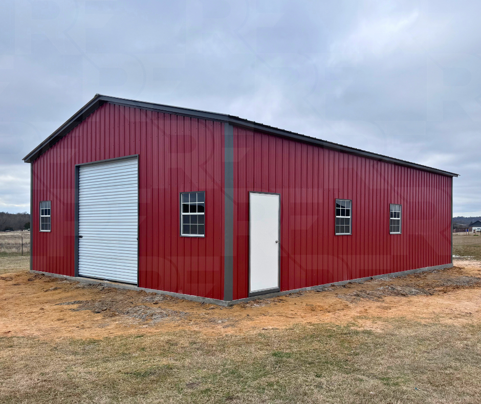 Red metal storage building with a 10x10 white roll-up door and four windows on a dirt patch in an open field.