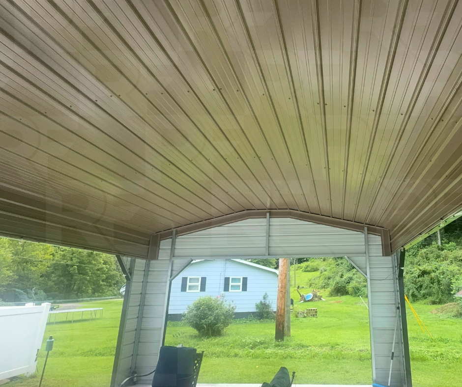 View from inside a metal garage overlooking a green yard and neighboring house with white siding.