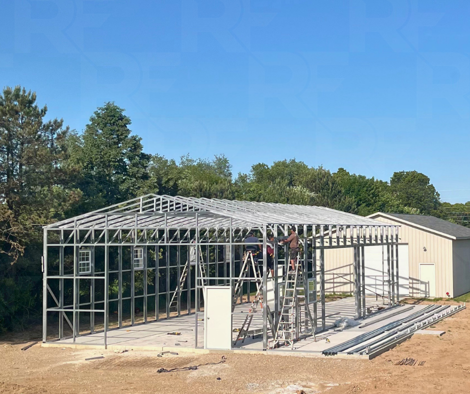 Construction of a metal building framework in progress outdoors with workers on ladders.