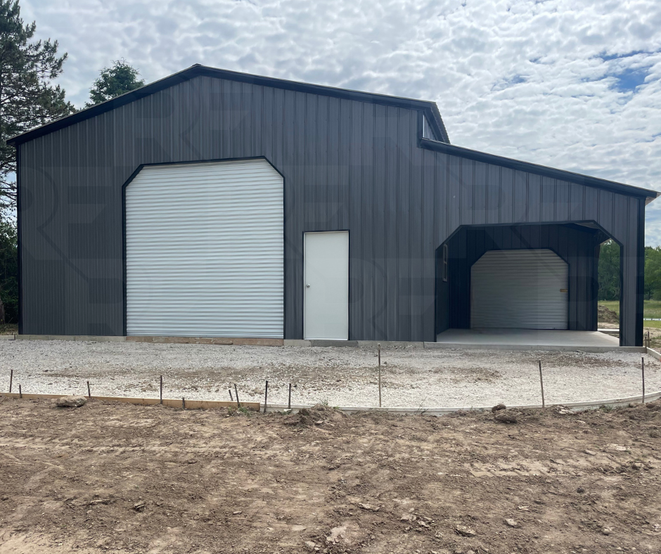 A modern metal building with two large garage doors and a side door, set on a gravel and dirt lot under a partly cloudy sky.
