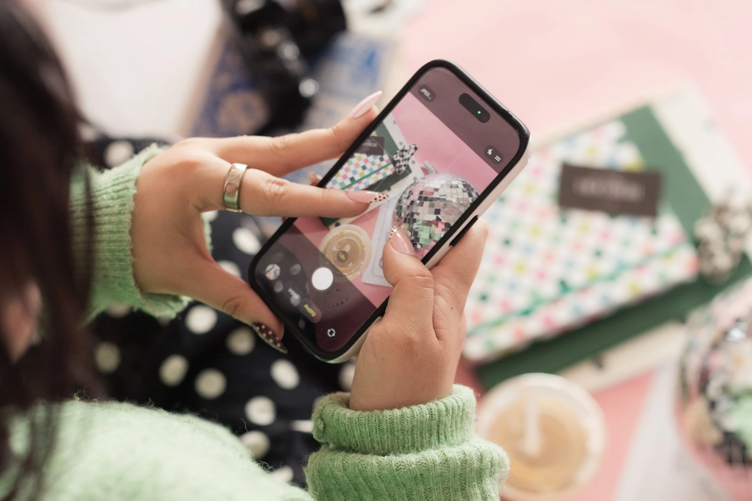 Person holding a smartphone, taking a photo of a colorful detail flat lay and a disco ball - content creation by Heirloom Media Co