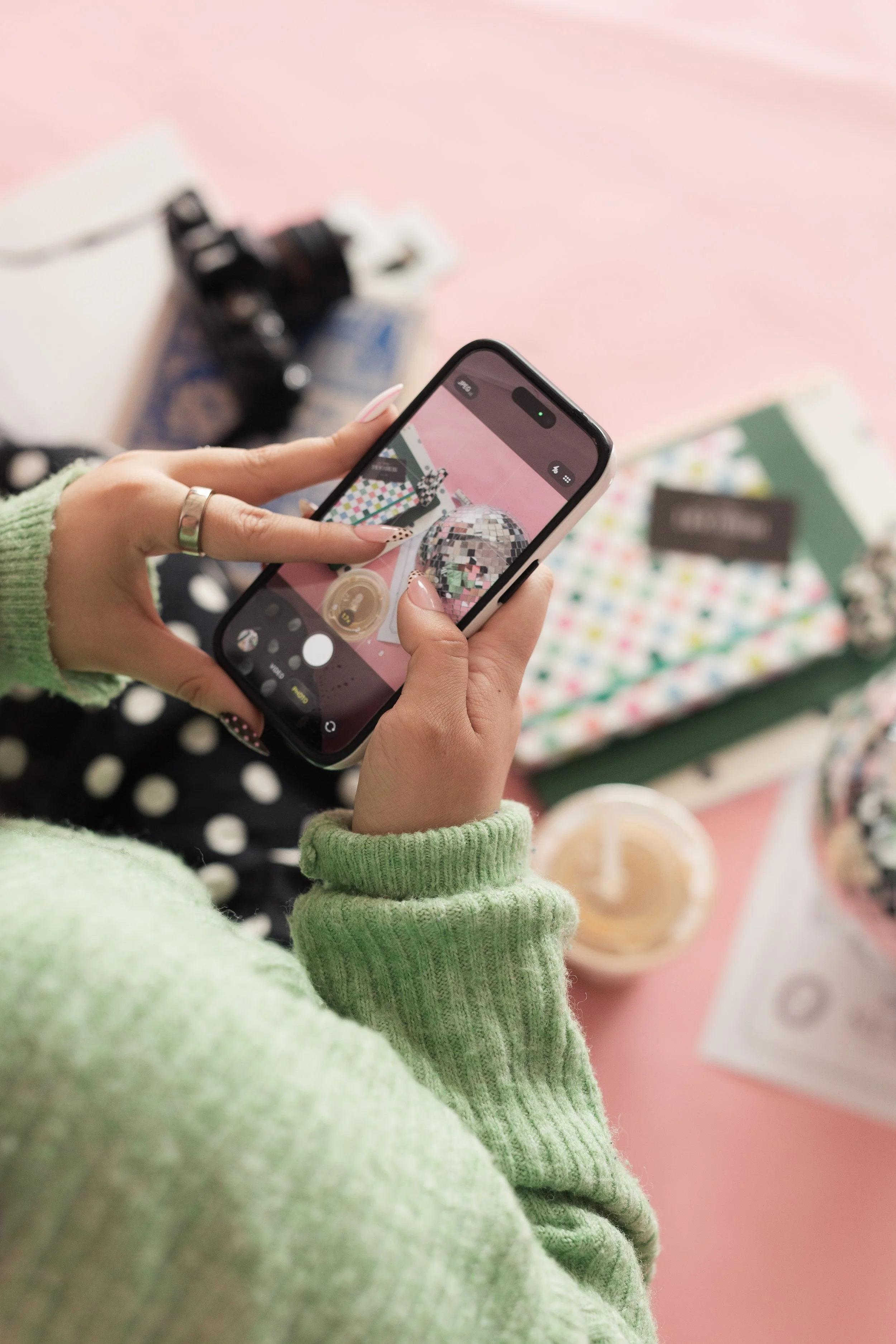 Person holding a smartphone with a festive scene on the screen, featuring a disco ball and colorful decor, and a pink background. Content creation by Heirloom Media Co