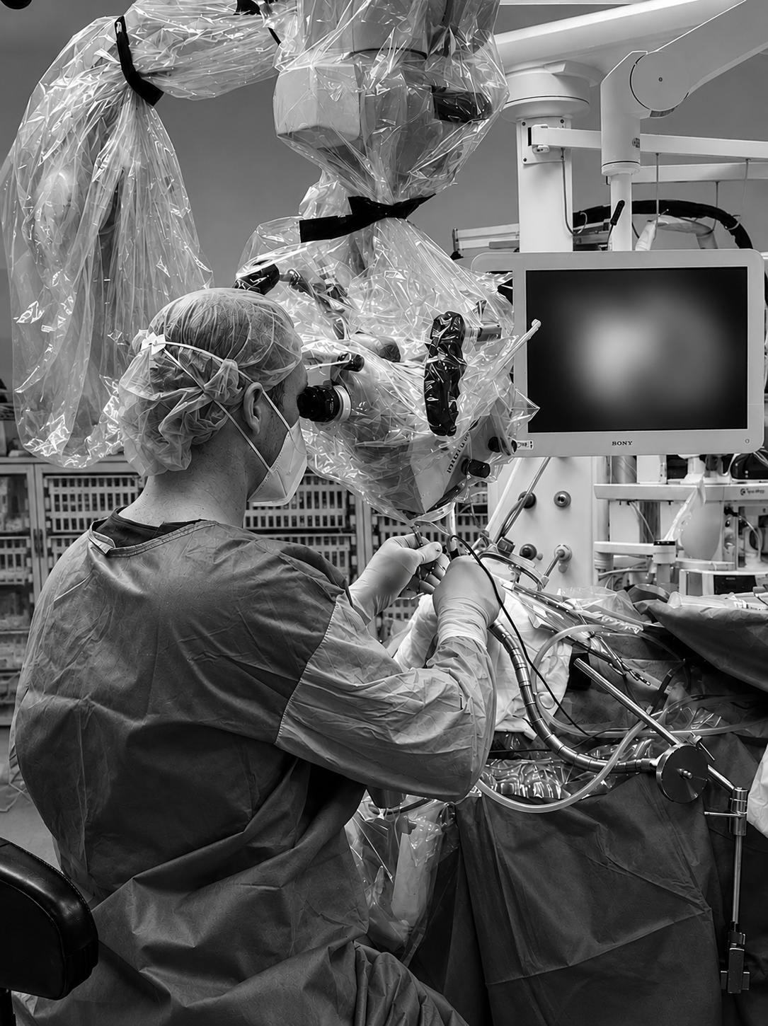 Medical professional in surgical gown, mask, and cap operating robotic surgical equipment in an operating room.