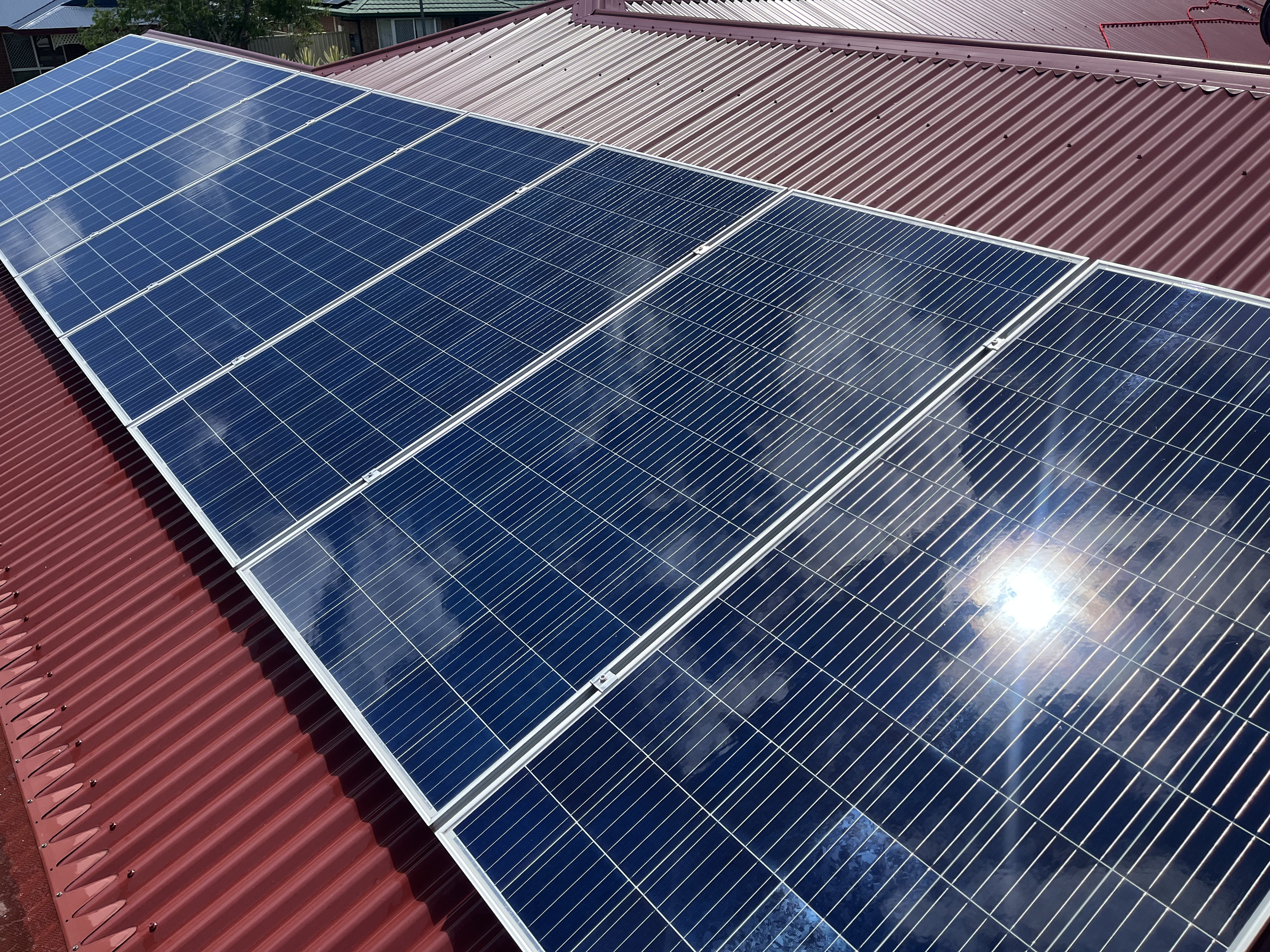 Several blue solar panels after being cleaned on a red metal roof, reflecting the sky and clouds.