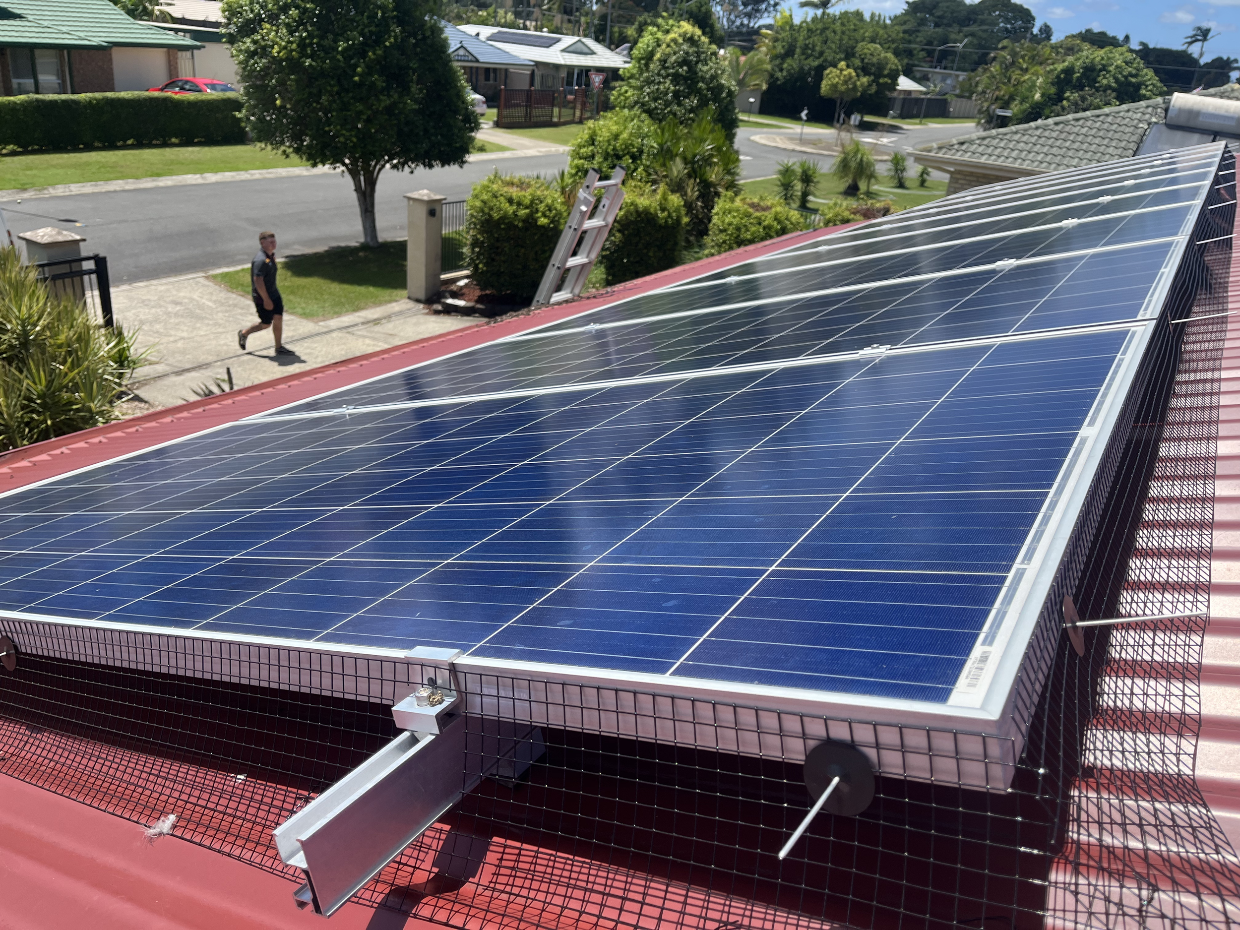 Solar panels cleaned on a red roof during sunny weather with a suburban neighborhood in the background.