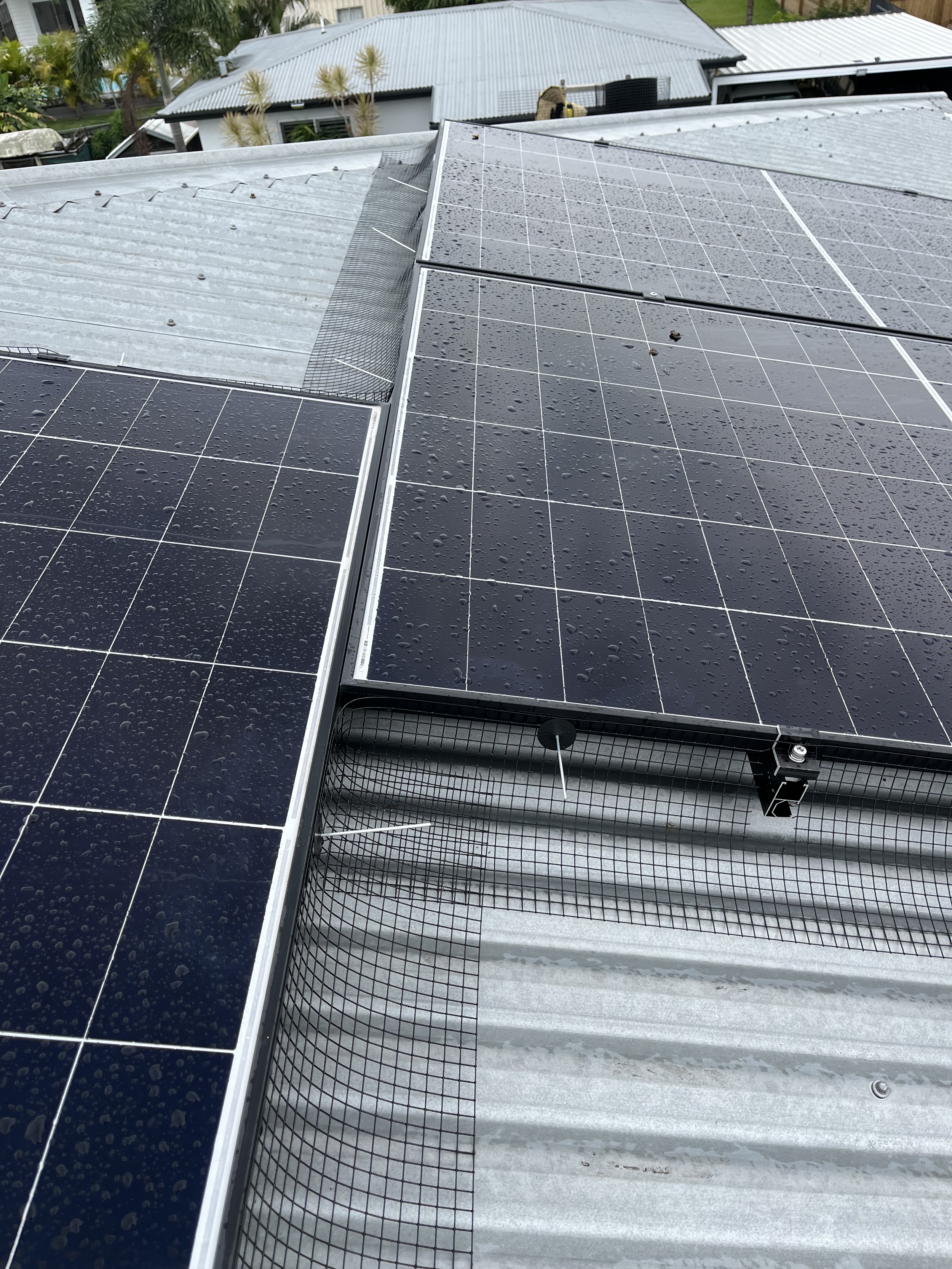 Solar panels installed on a corrugated metal roof, with raindrops on the panels and surrounding area.