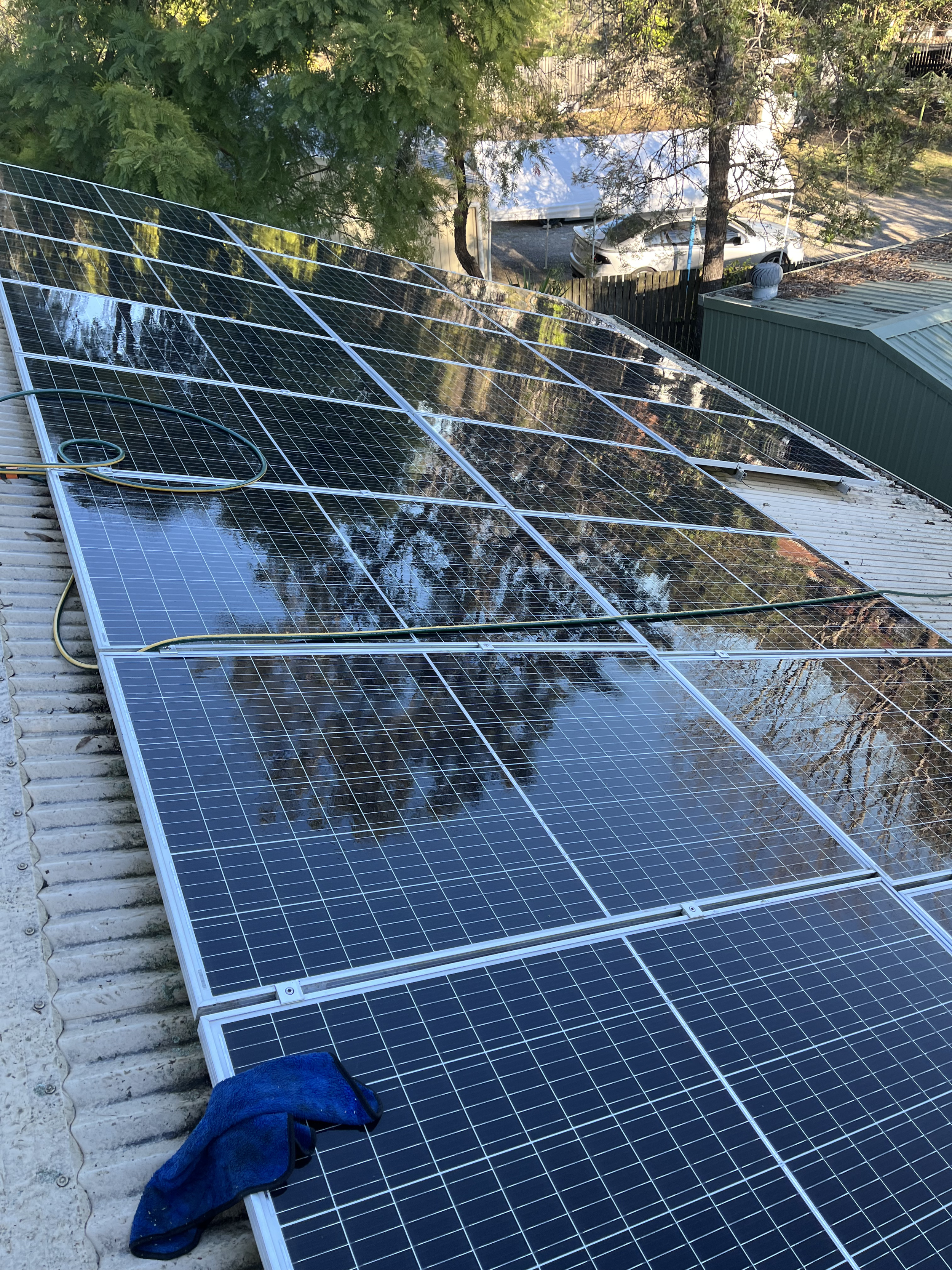 Solar panels installed on a rooftop, reflected in the panels are trees and the sky.