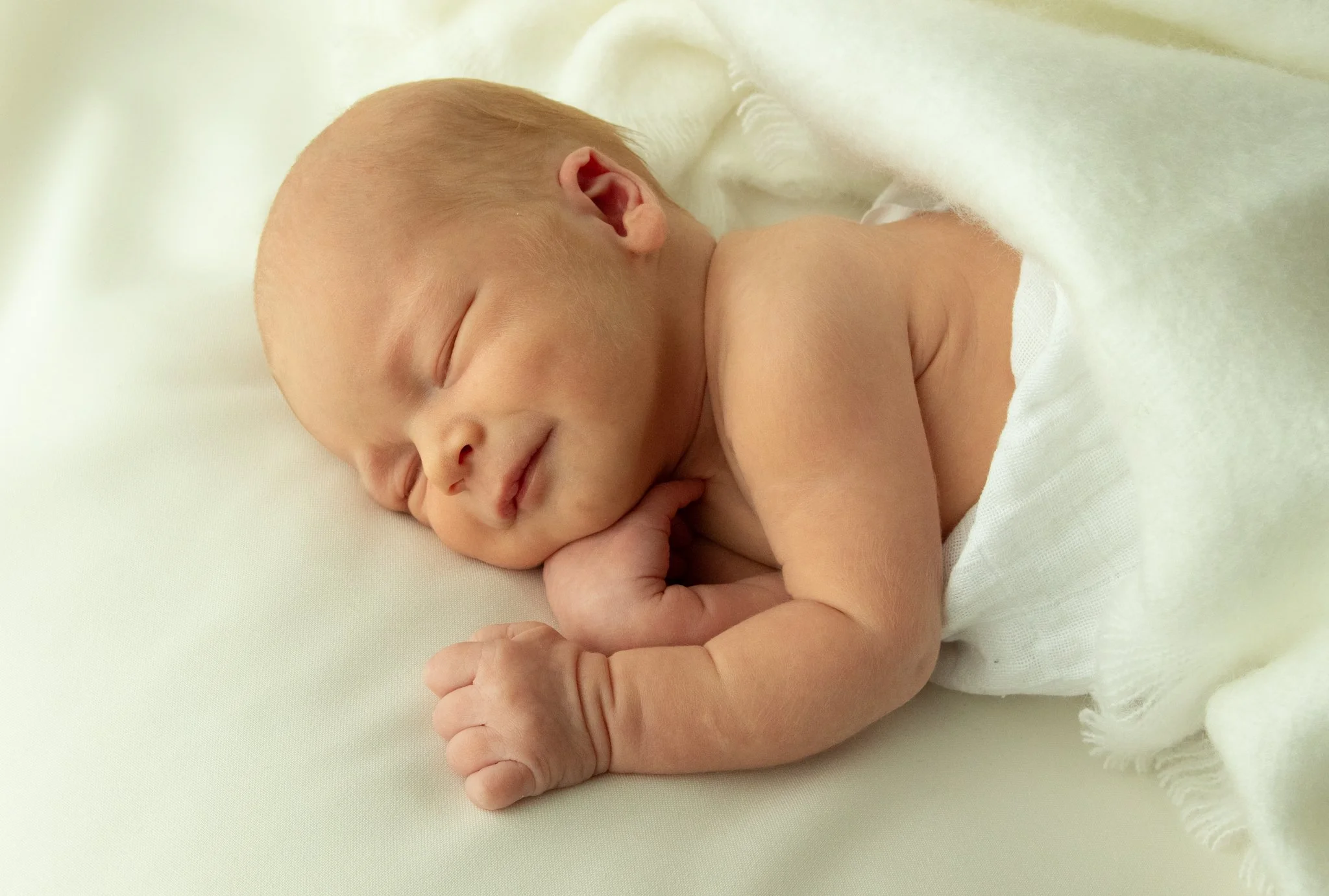 Vastasyntynyt vauva nukkuu pehmeällä alustalla – luonnonvalossa toteutettu newborn-kuvaus lämpimässä sävyssä