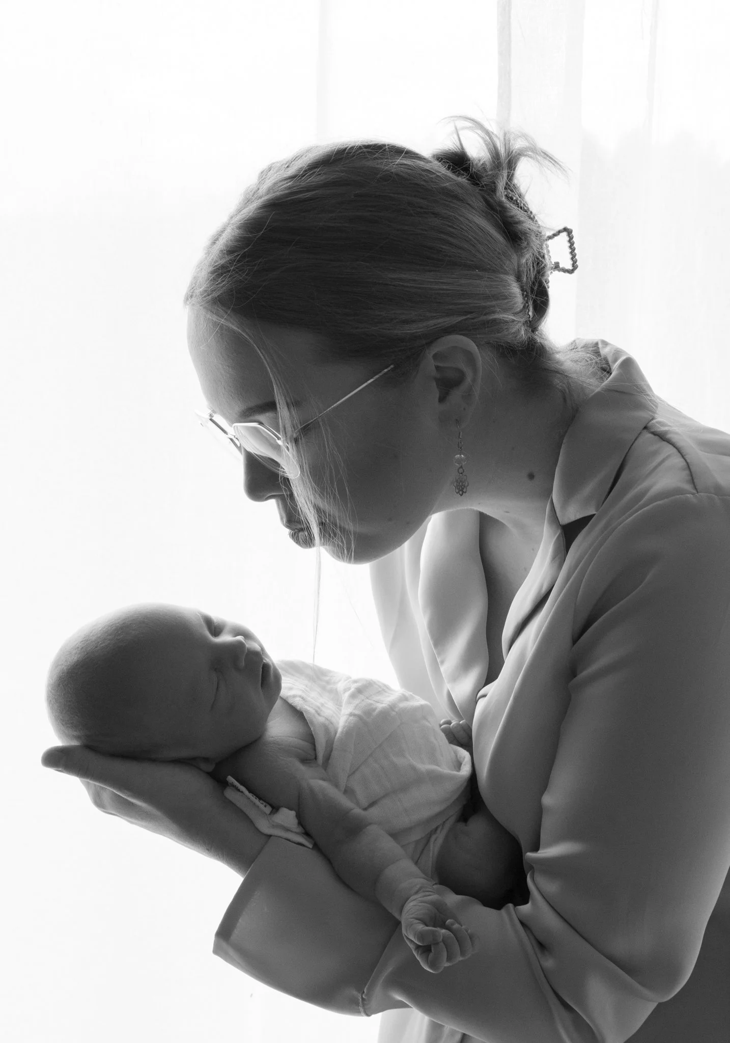 Äiti katsoo vastasyntynyttä vauvaa sylissään – herkkä perhe- ja newborn-kuvaus ajattomassa mustavalkoisessa tyylissä