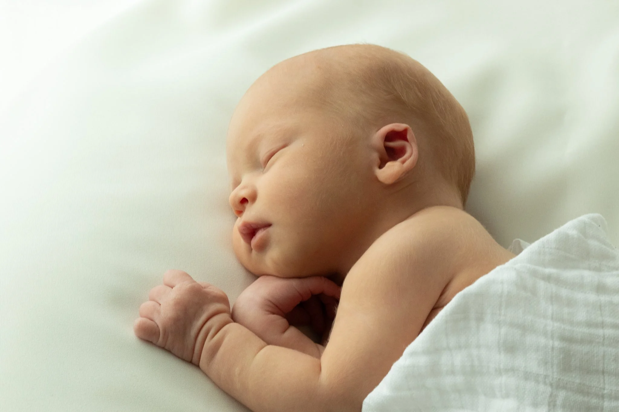 Vastasyntynyt vauva nukkuu pehmeällä alustalla – luonnonvalossa toteutettu newborn-kuvaus lämpimässä sävyssä