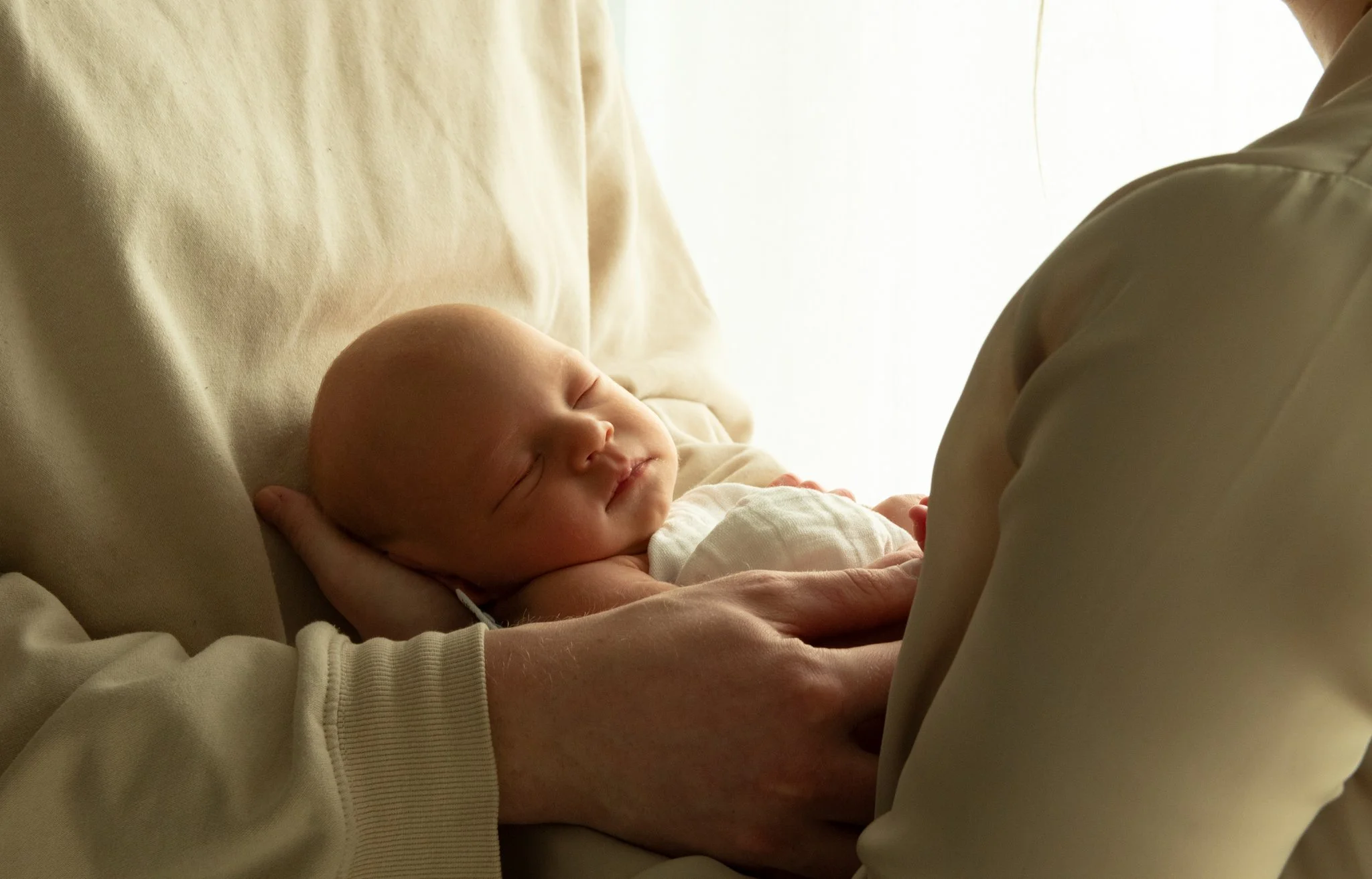 Vastasyntynyt vauva vanhemman sylissä – lämmin ja luonnollinen perhe- ja newborn-kuvaus pehmeässä valossa