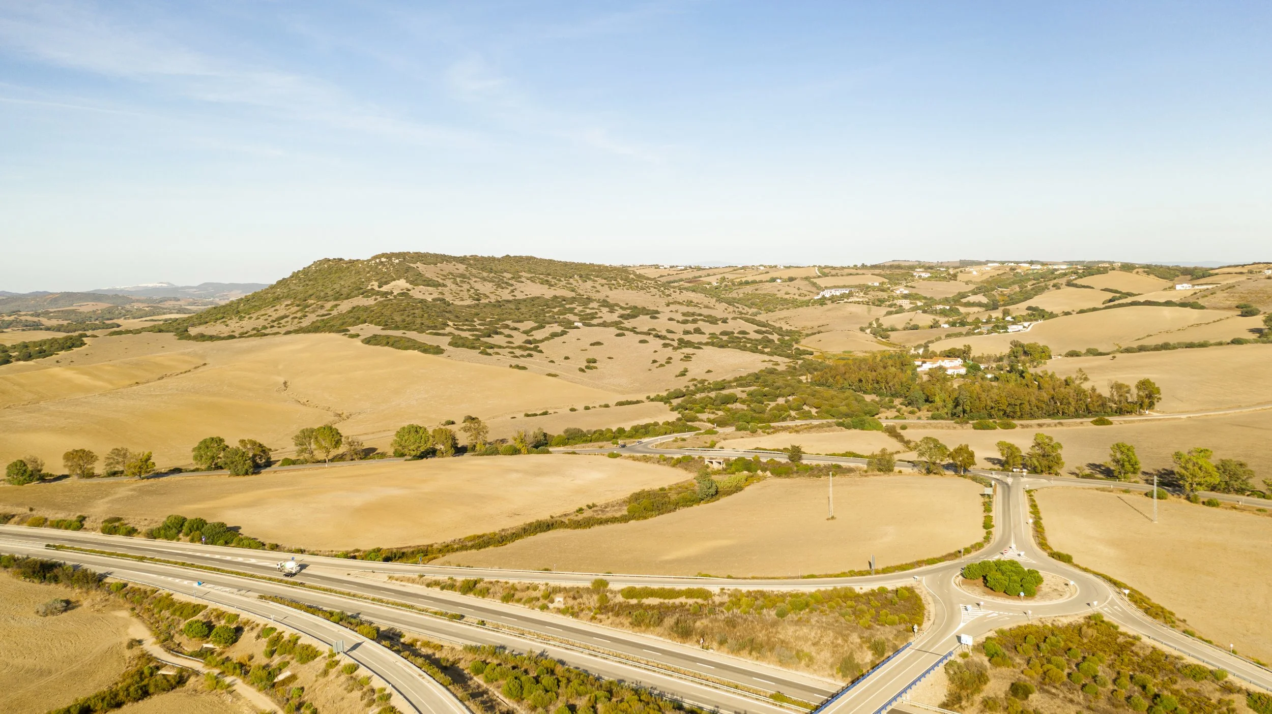 Aerial view of rolling hills and open fields in a rural area with a highway and roundabout