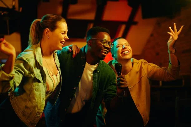 Group of three friends laughing and singing with a microphone in a lively indoor setting.