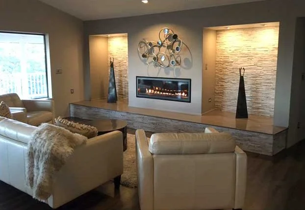 Living room with a modern fireplace, decorative wall art, two tall vases, and white sofas with a furry throw, illuminated by natural and accent lighting.